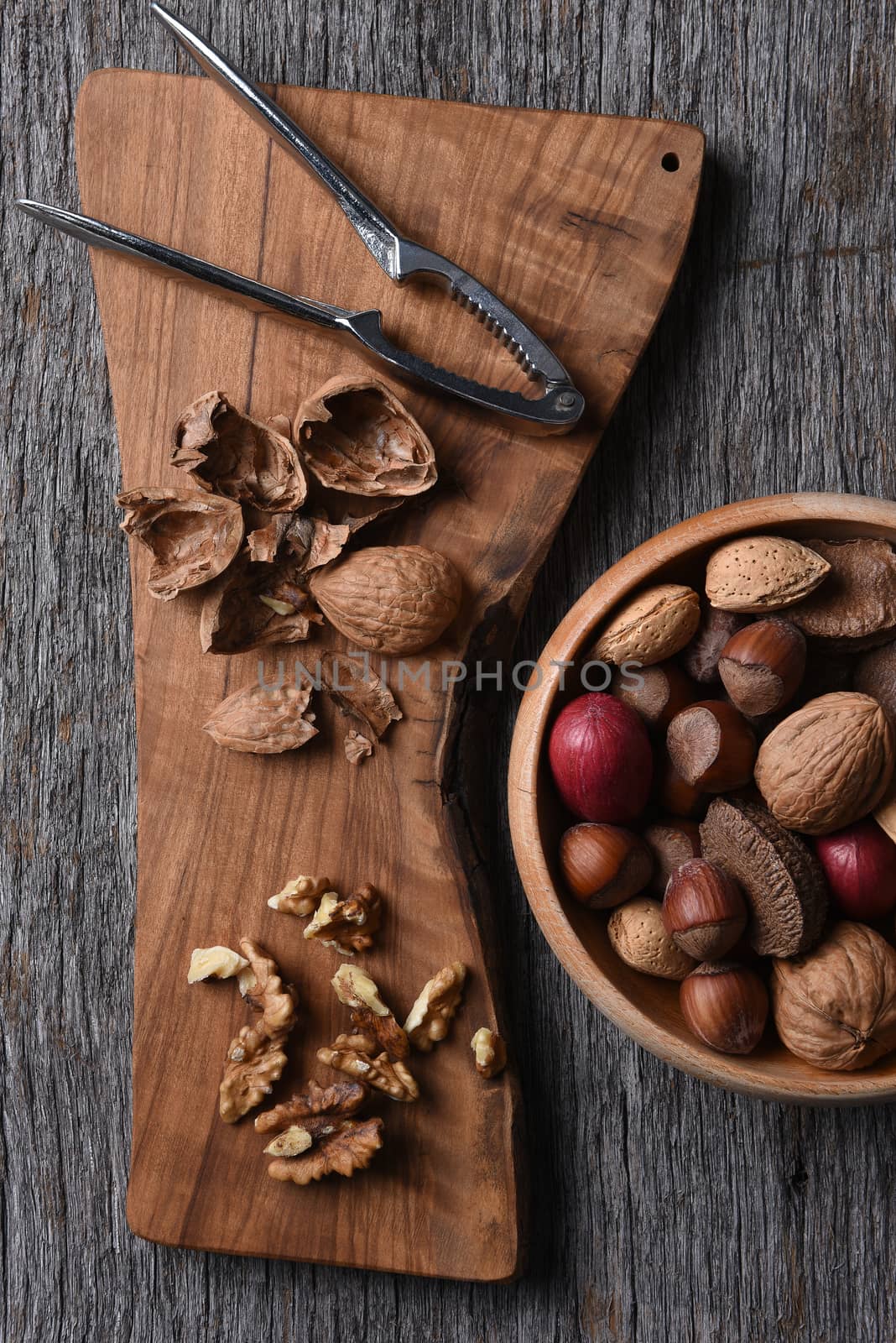 Cracked walnuts and nutcracker on a cutting board with a bowl of mixed whole shelled nuts.