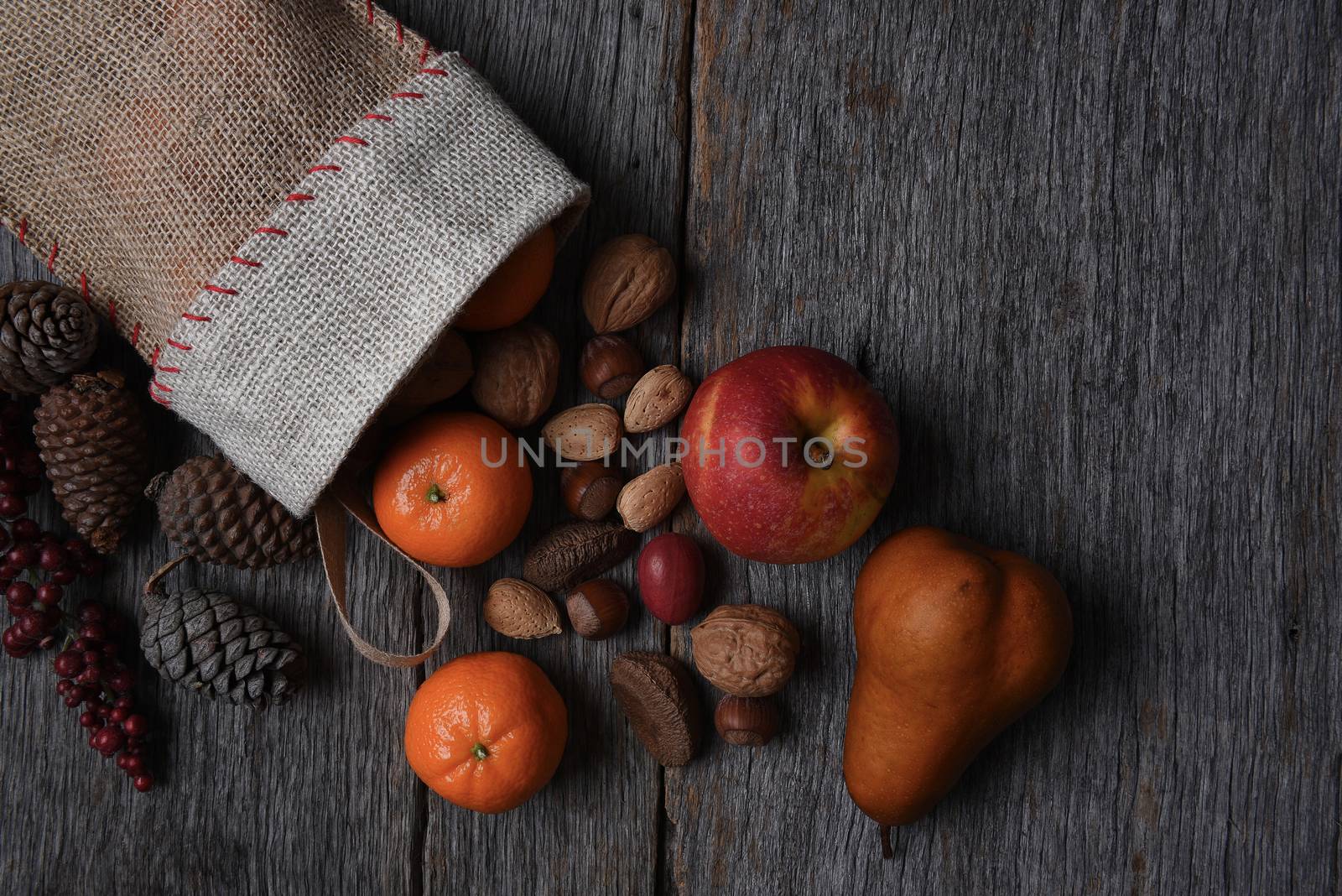 Top view of an old fashioned Christmas Stocking filled with fruits and nuts on a rustic wood table with the contents spilling out.