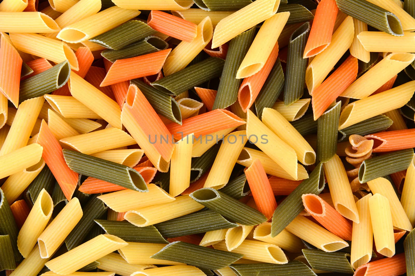 Tri-color penne pasta, filling the frame. Tomato, spinach and wheat pastas are shown, horizontal format.