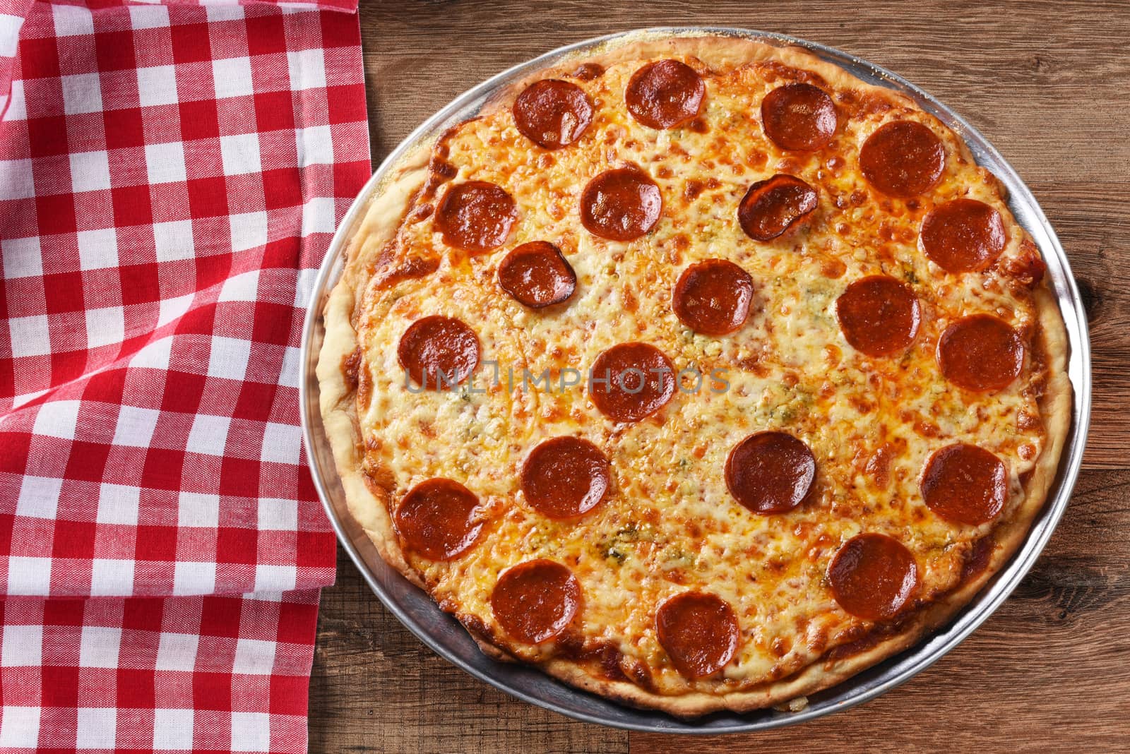 Fresh Homemade Pepperoni Three Cheese Pizza on a red checkered table cloth on a wood table with copy space, horizontal format. 
