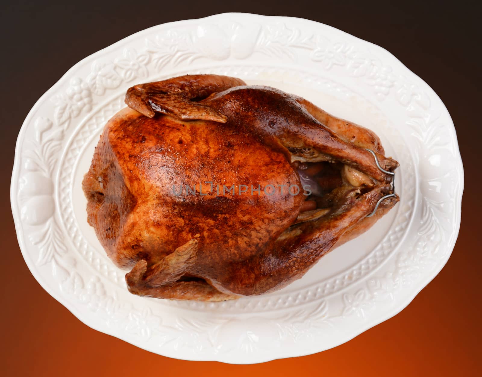 Overhead of a roasted Thanksgiving turkey on a white platter. Horizontal format on a light to dark warm background.