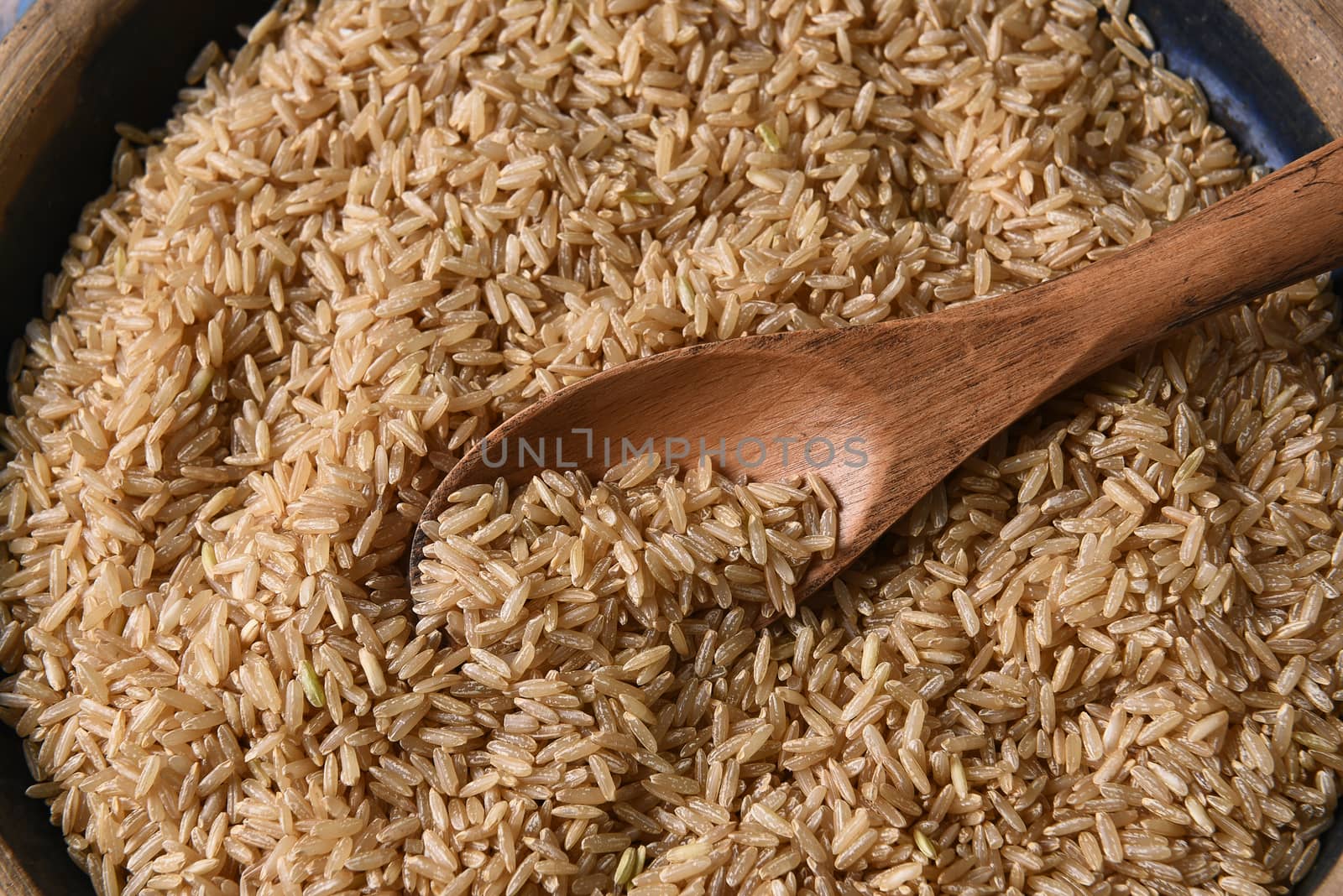 Closeup of a wooden spoon in a bowl full of brown rice. 