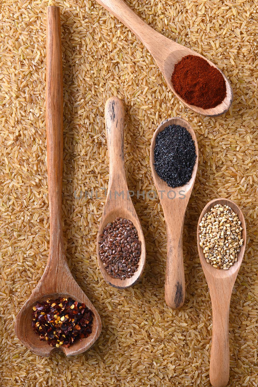Top view of grains and spices on wooden spoons atop a bed of brown rice.
