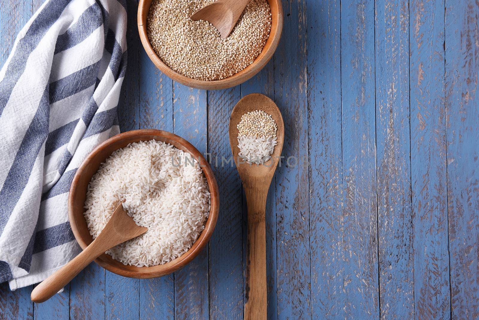Wood Bowls of Rice and Quinoa on a rustic blue table with a kitchen towel and a wooden spoon. Horizontal format with copy space.