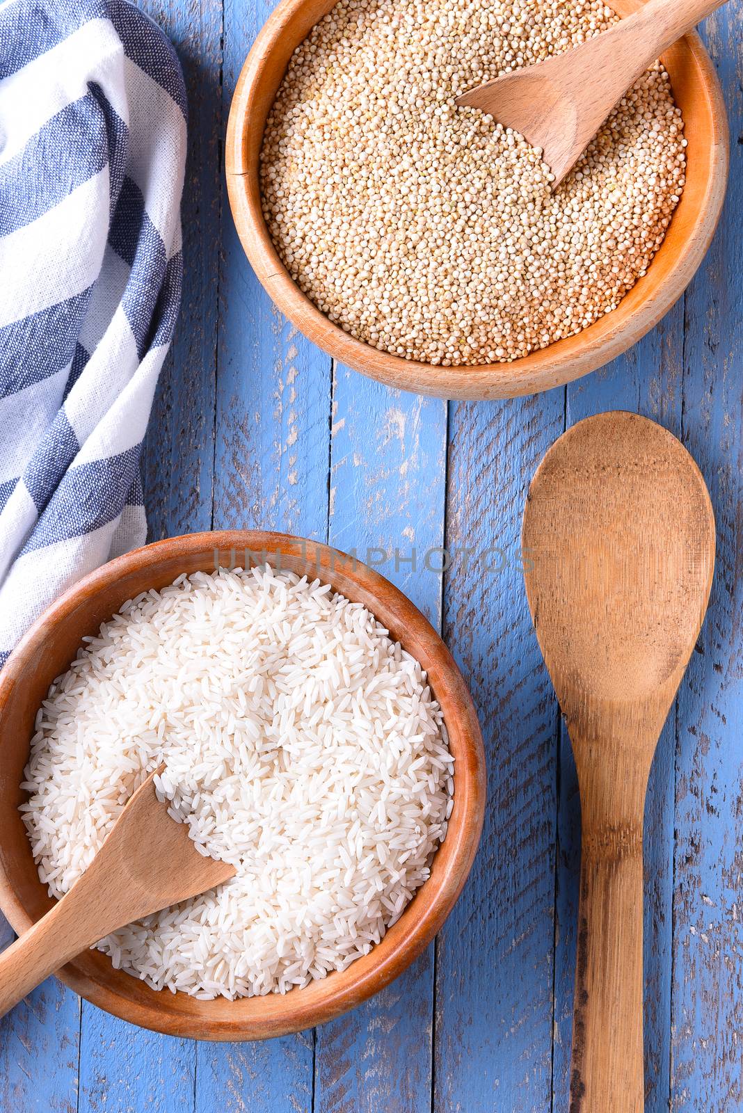 Top view of rice and quinoa in wooden bowls on a blue wood table.