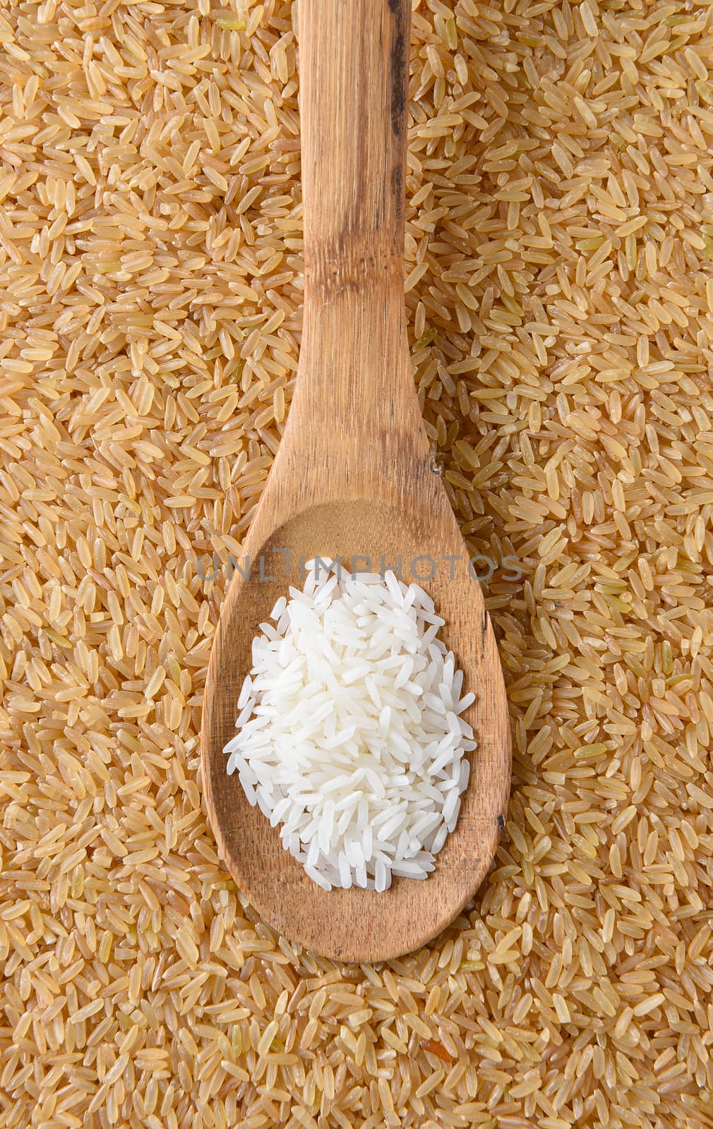 Top view of a wooden spoon with uncooked white rice. The spoon is on a background of brown rice filling the frame.