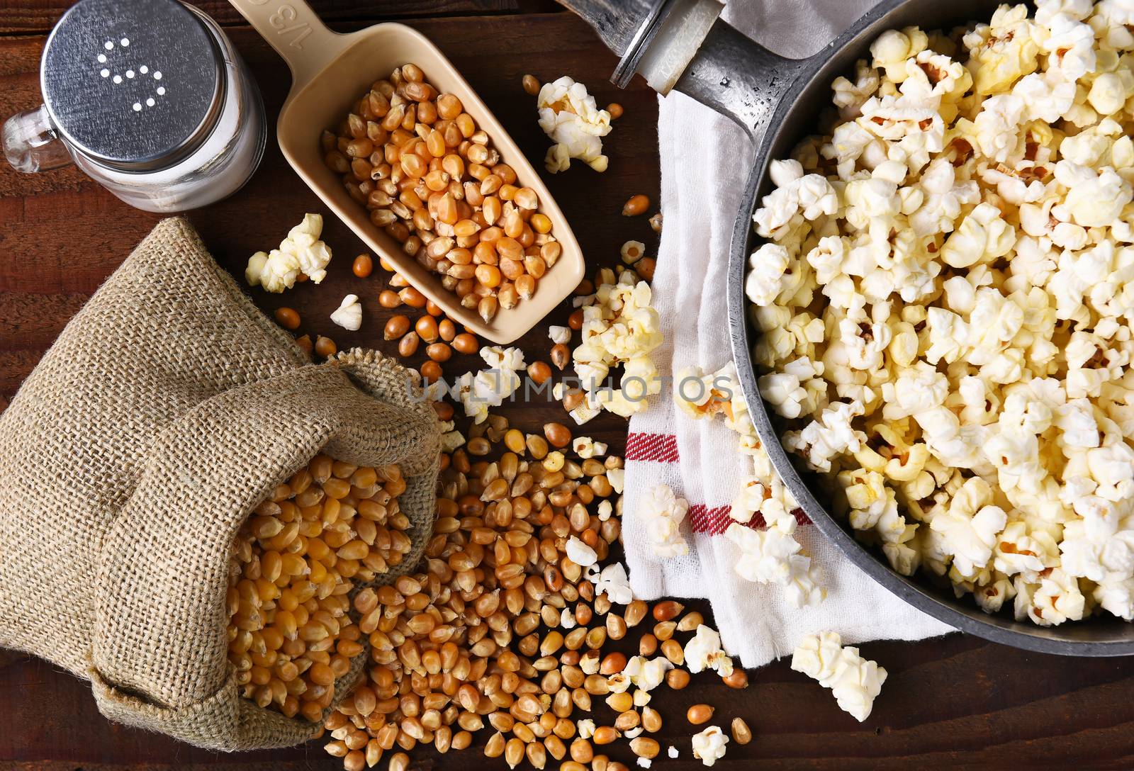 Top view of a pot full of freshly popped popcorn with salt and unpopped kernels on the side. 