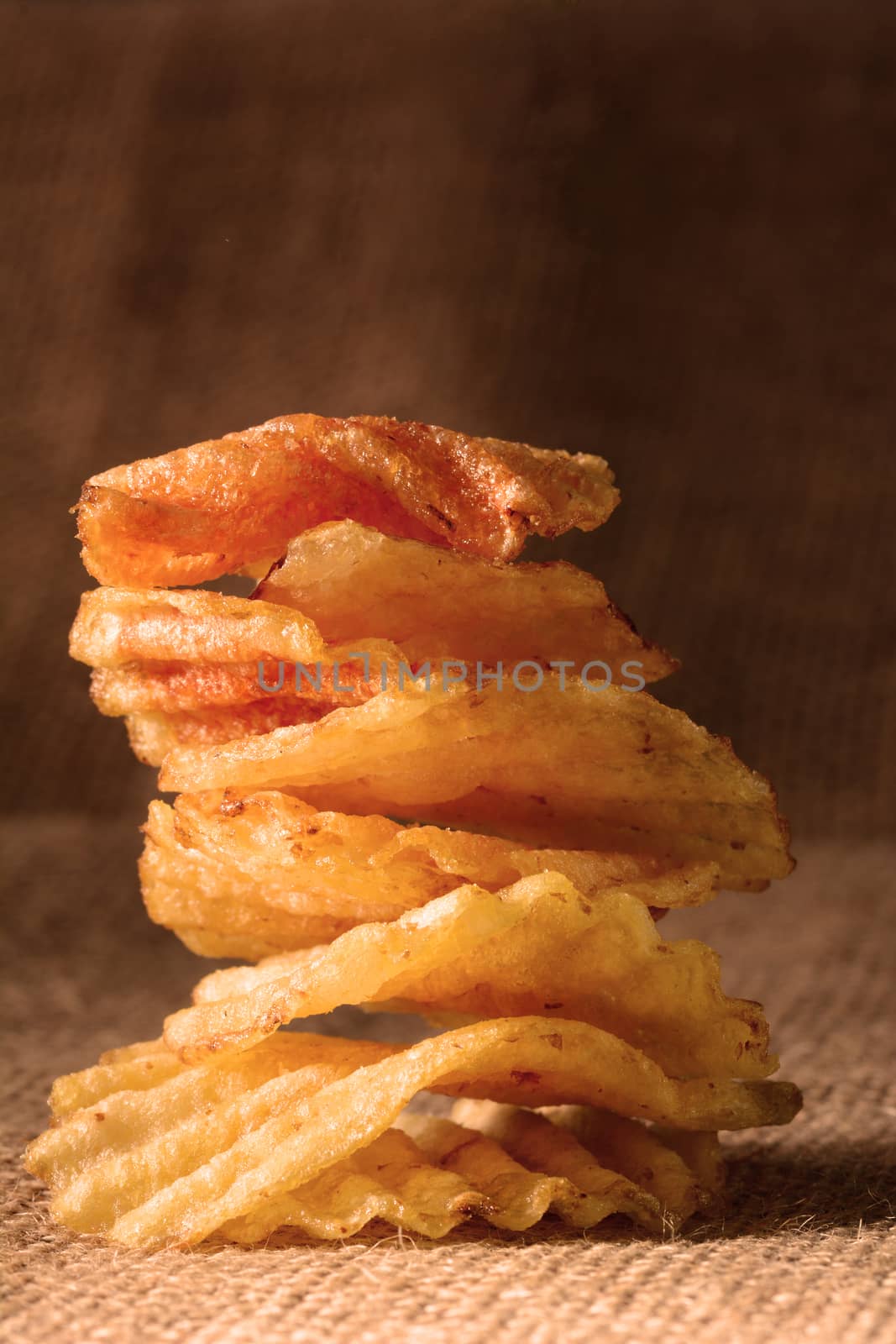 A stack of potato chips with warm side light. Vertical format on a burlap surface.