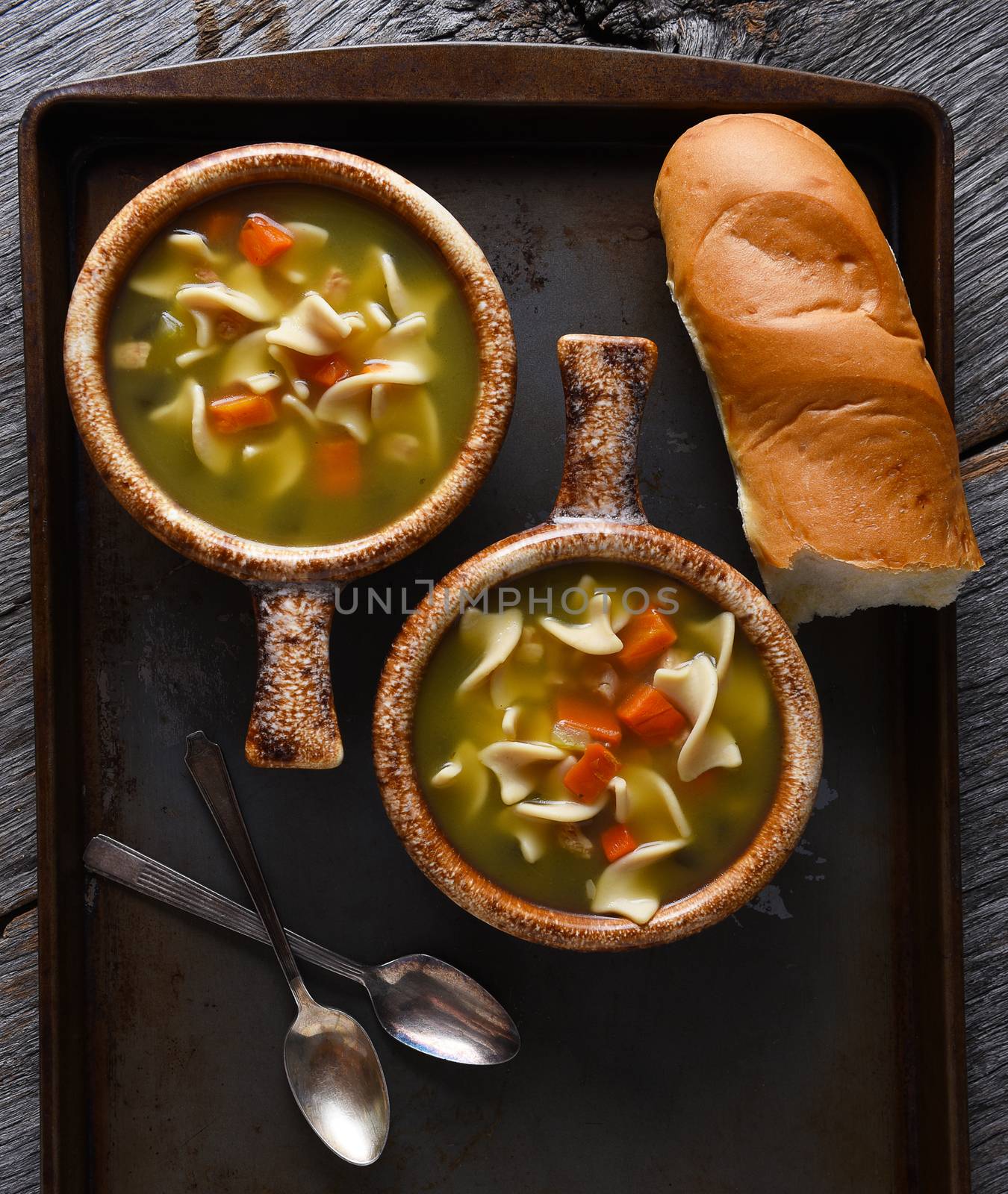 Two fresh homemade bowls of Chicken Noodle Soup with a baguette and spoons. Closeup in vertical format.