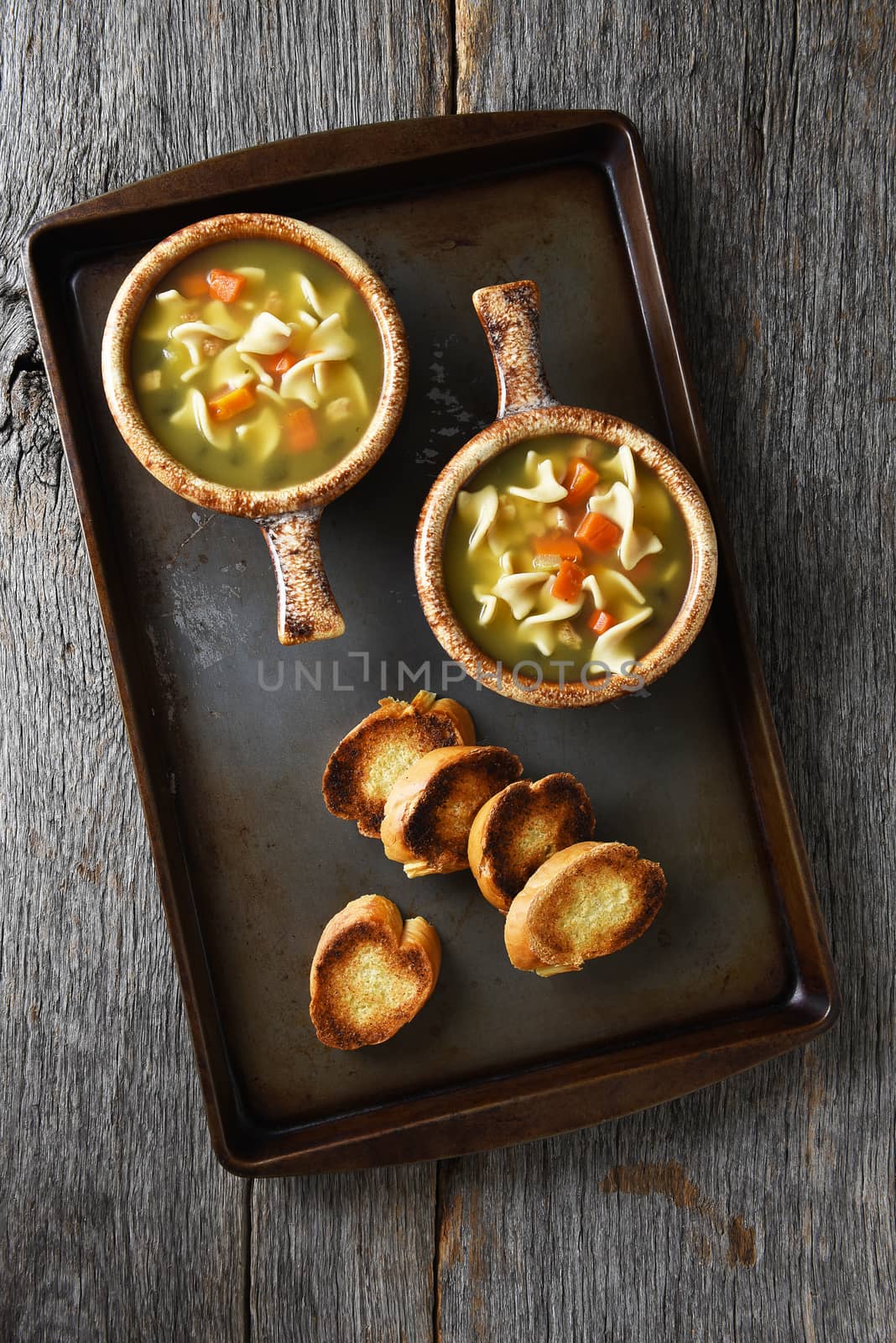 Two fresh homemade bowls of Chicken Noodle Soup with Garlic Toast on a metal baking sheet.