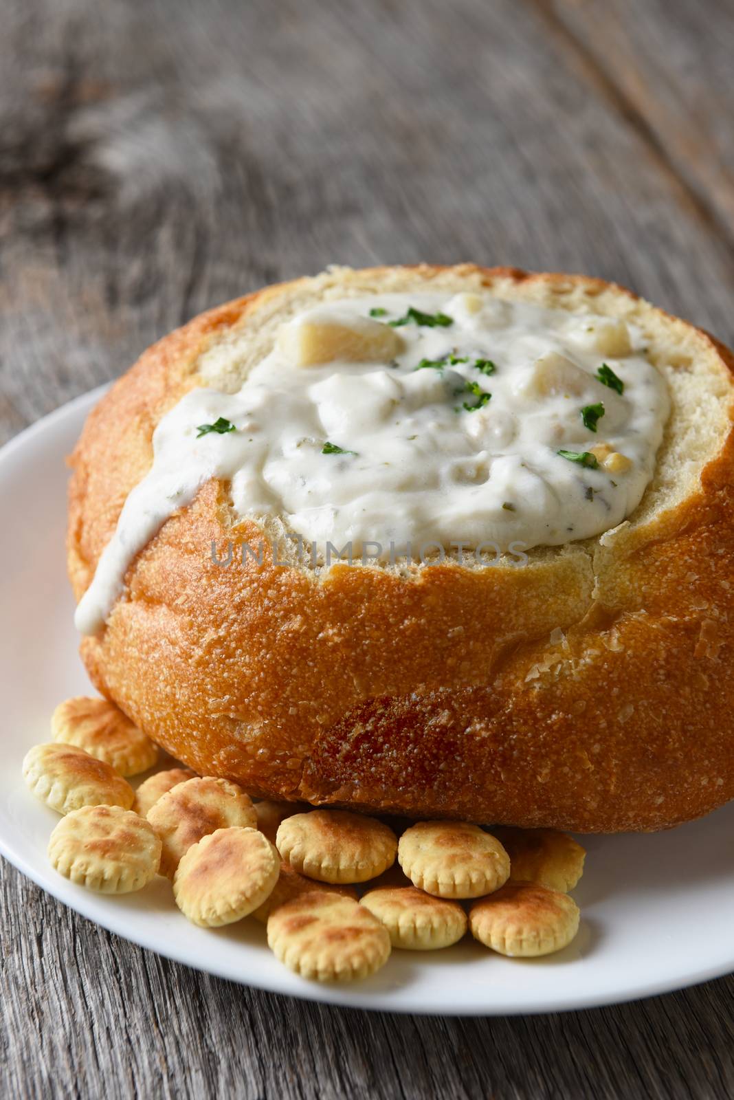 Closeup vertical of New England Style Clam Chowder in a bread bowl, with oyster crackers and copy space.