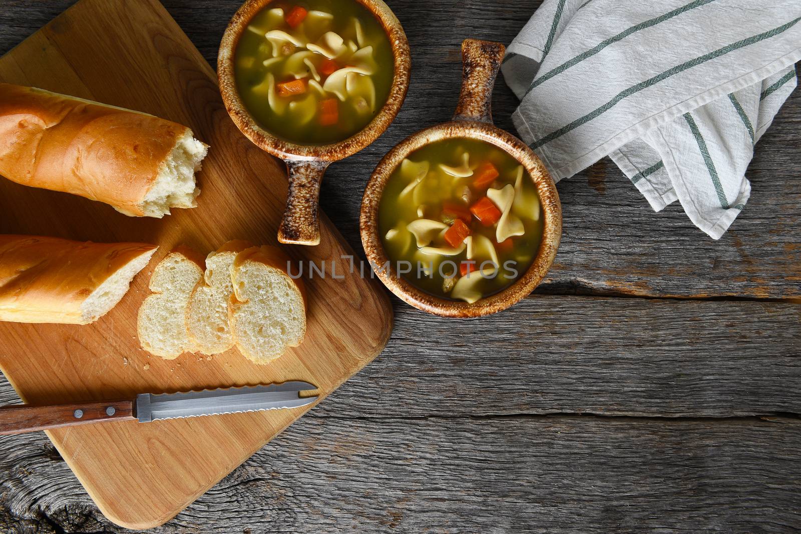 Top view of two bowls of homemade Chicken Noodle Soup with fresh baked loaf of bread. Horizontal with copy space.