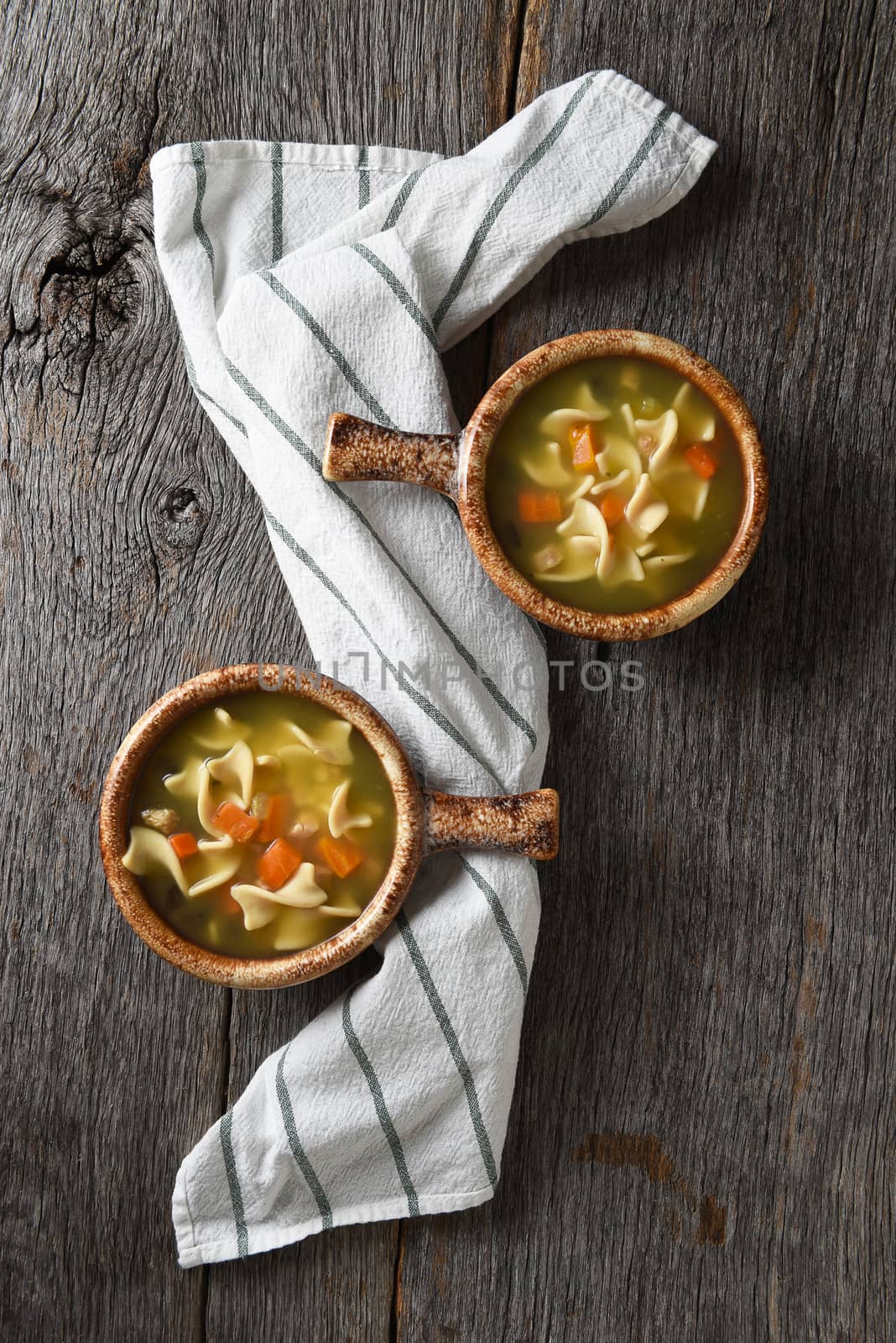Flat lay with two bowls of homemade Chicken Noodle Soup on a rustic wood table with a kitchen towel.