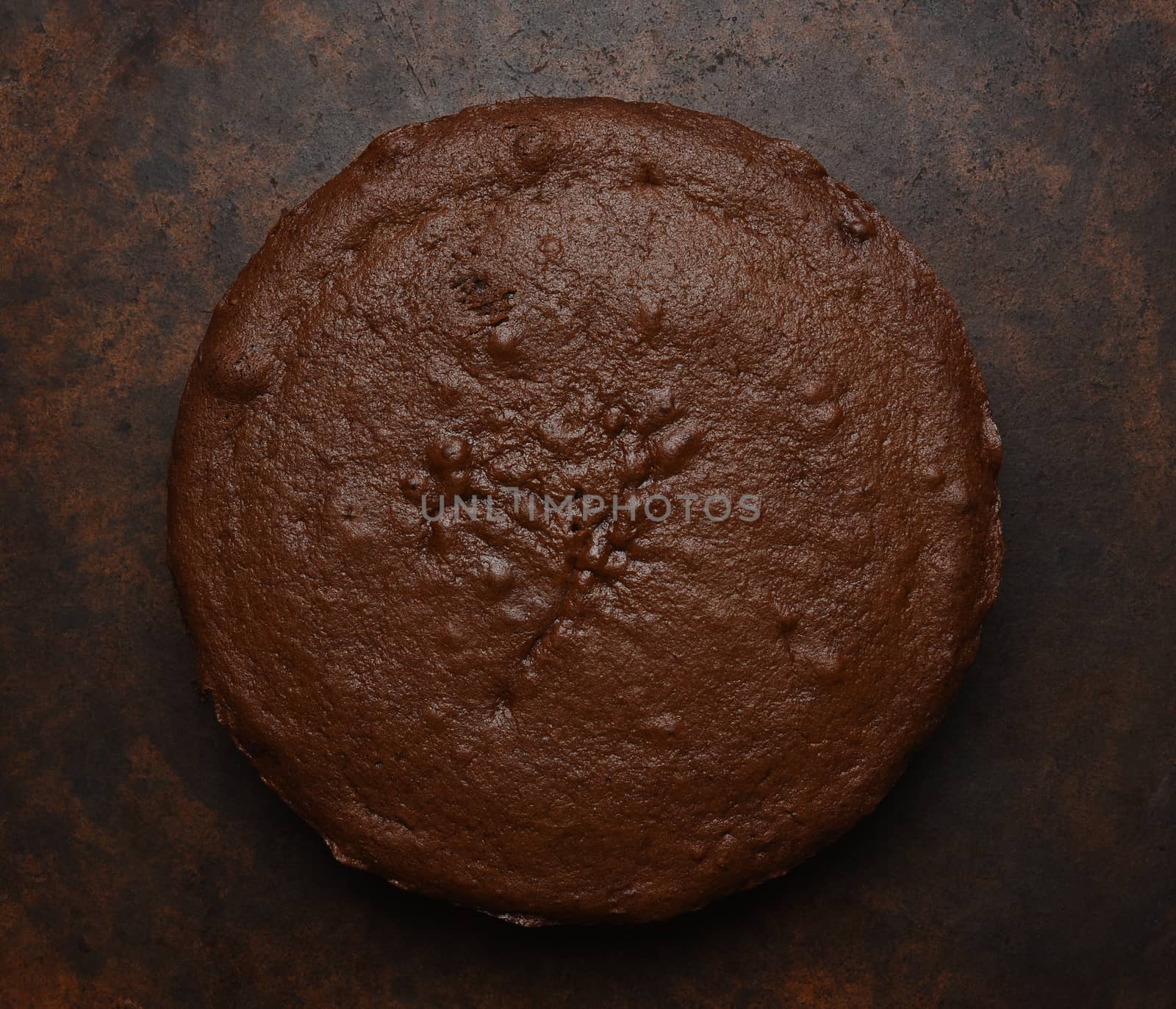 Flat lay of a single layer chocolate cake on a dark brown mottled background. 