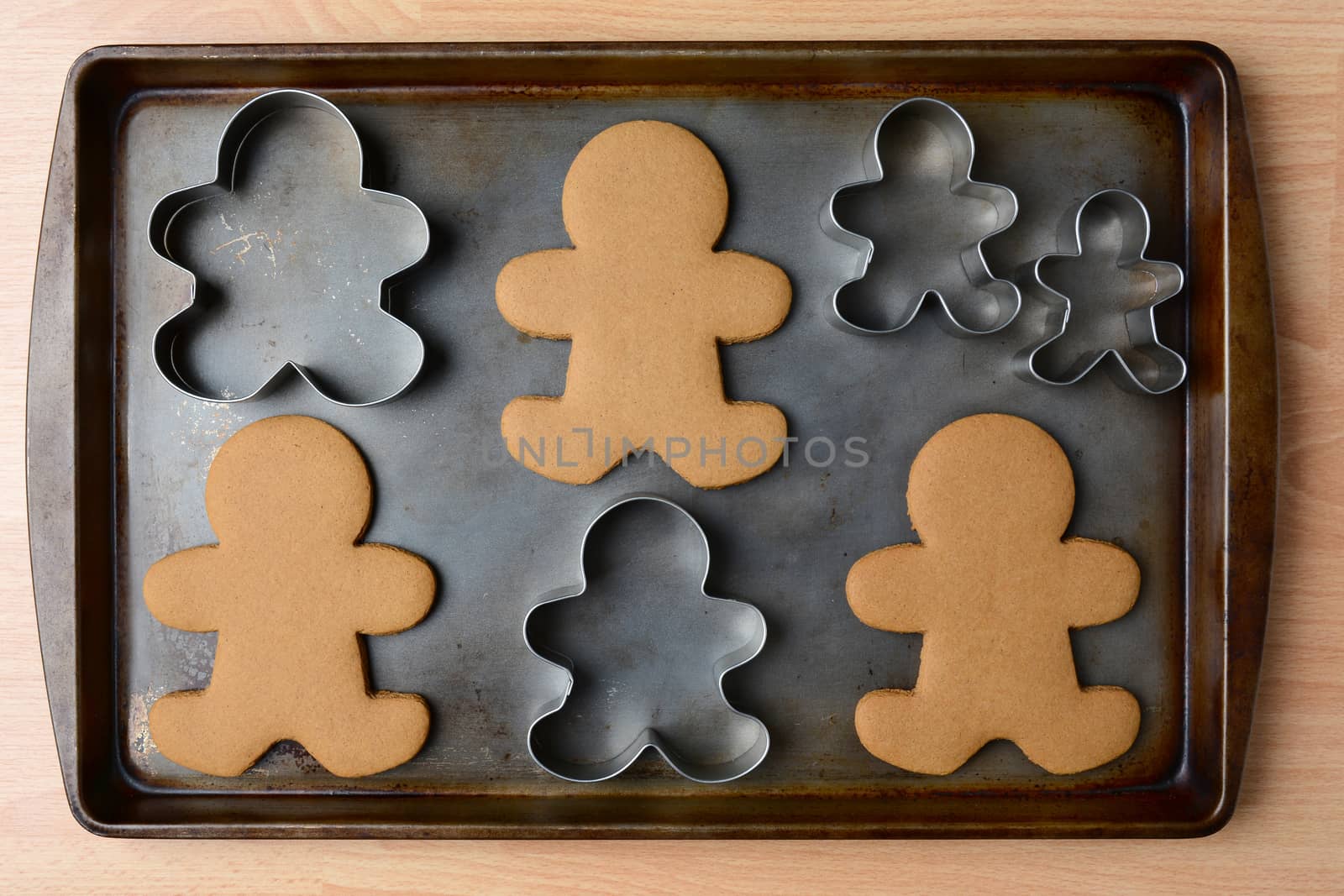 High angle shot of an old baking sheet with Christmas gingerbread man cookies and cookie cutters. Horizontal format on wood kitchen table.