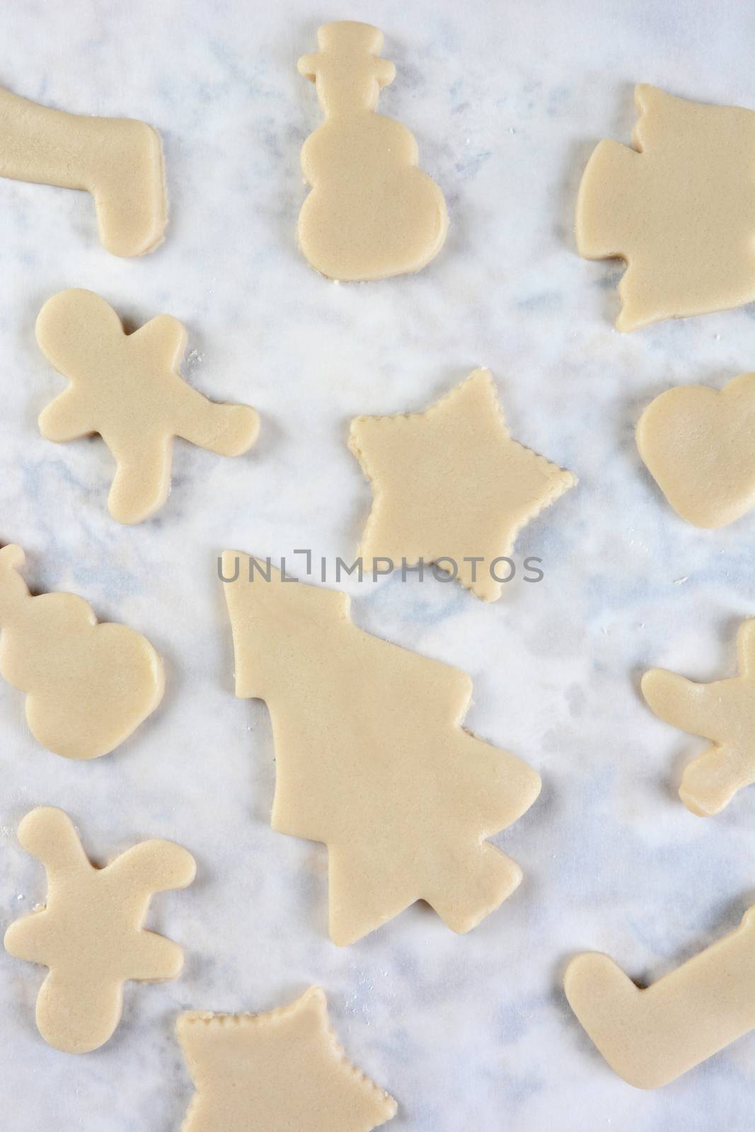 High angle view of a group of raw dough Christmas cookie shapes on parchment paper. Vertical format.