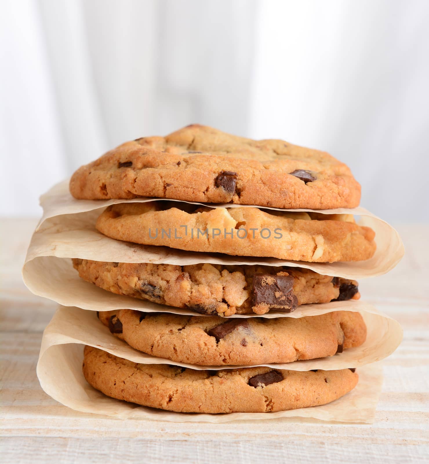 Closeup of a stack of fresh baked cookies Chocolate Chip, Oatmeal Raisin, White Chocolate Chip cookies on parchment paper.
Square format on a rustic white kitchen table.
