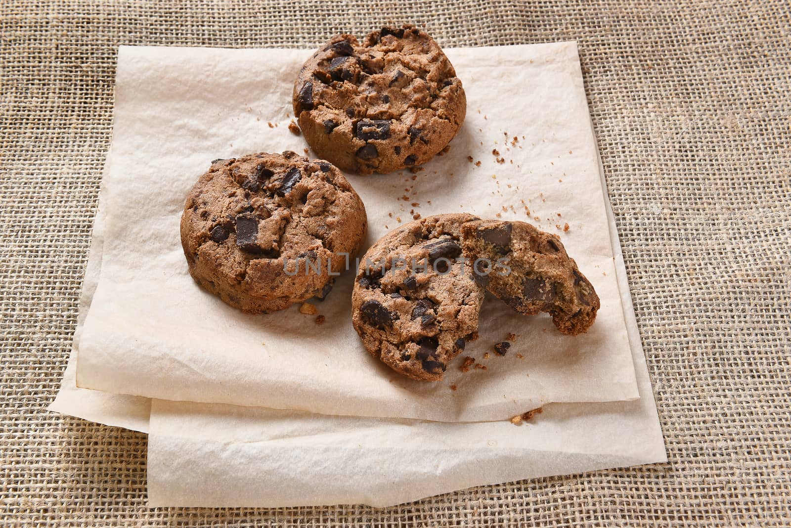 Closeup of a pile of chocolate chocolate chunk chip cookies on parchment paper and burlap.