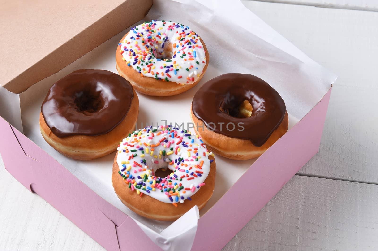 Closeup of a pink bakery box with four fresh donuts, two chocolate and two frosted with sprinkles. 