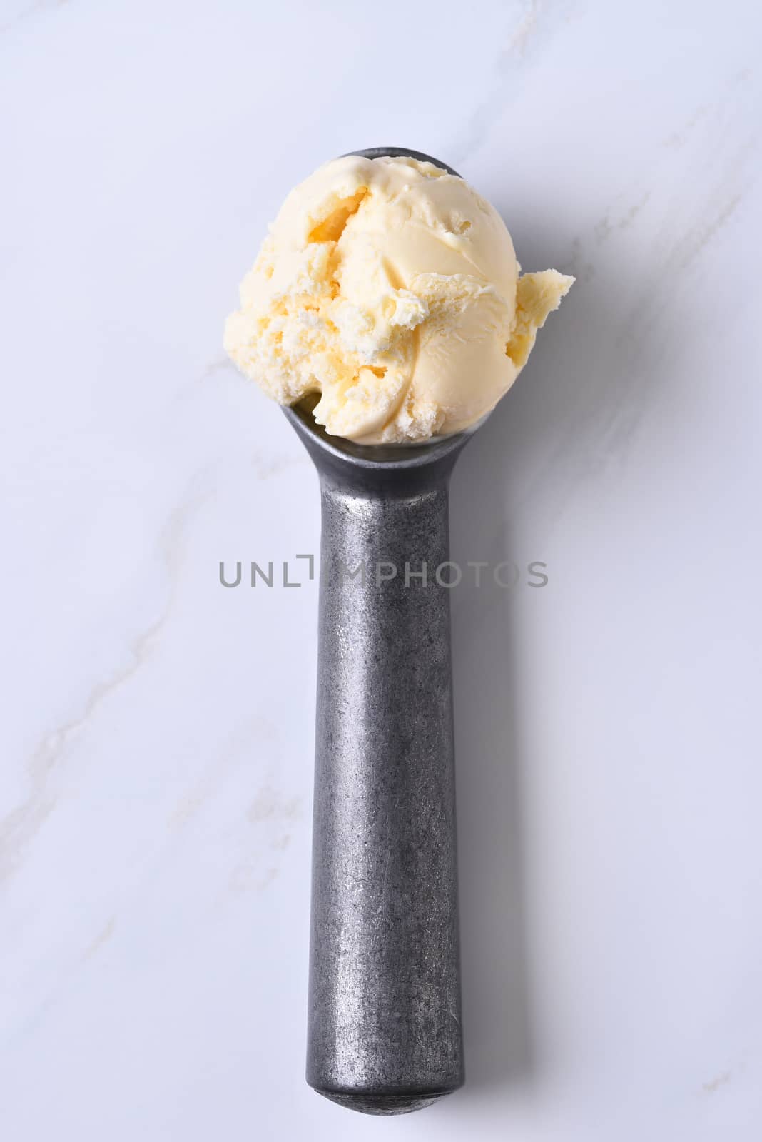 Top view of an ice cream scoop with vanilla ice cream. Vertical format on a marble counter top.