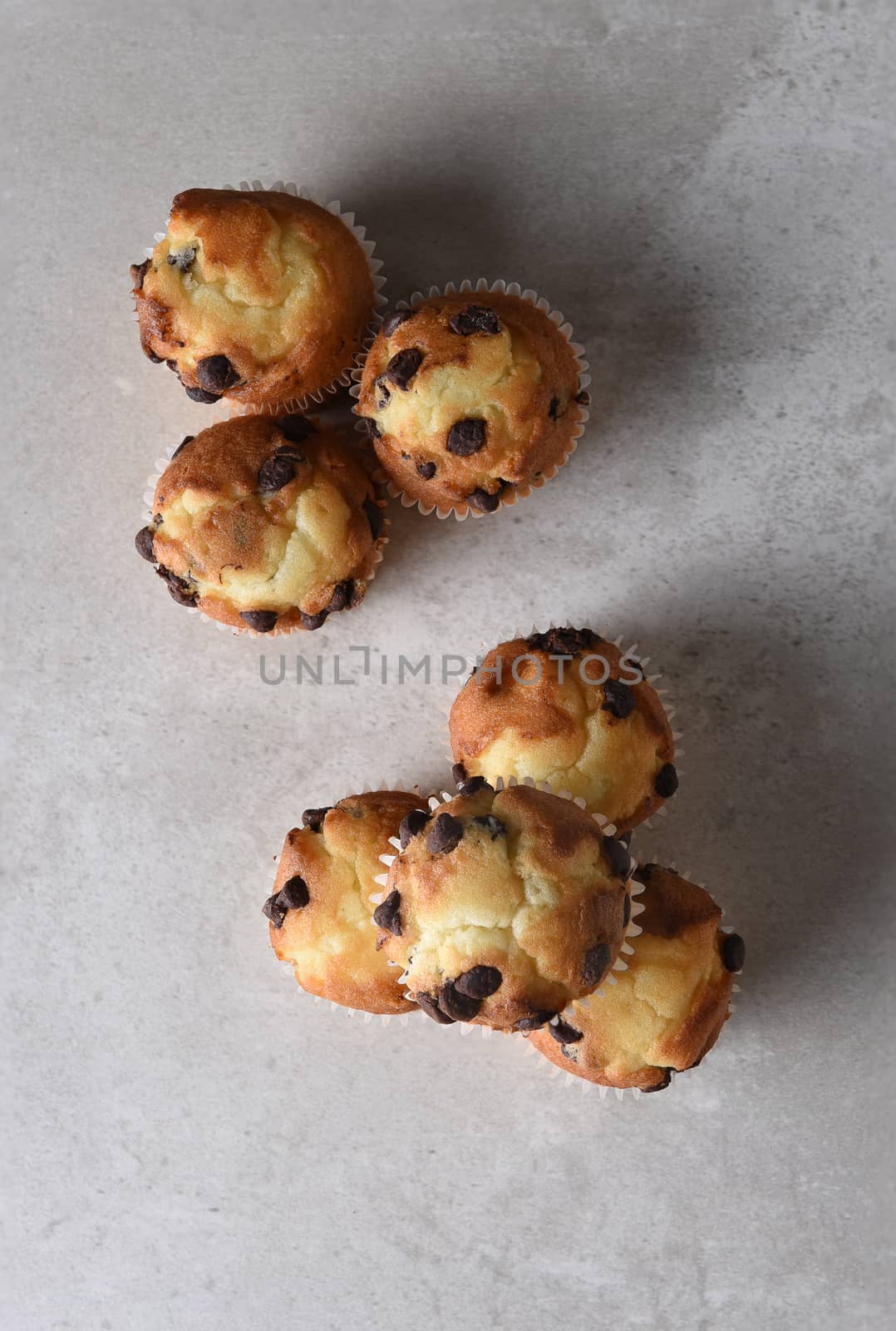 Top shot of a croup of fresh baked chocolate chip mini muffins on a light gray kitchen counter. Vertical format with copy space,