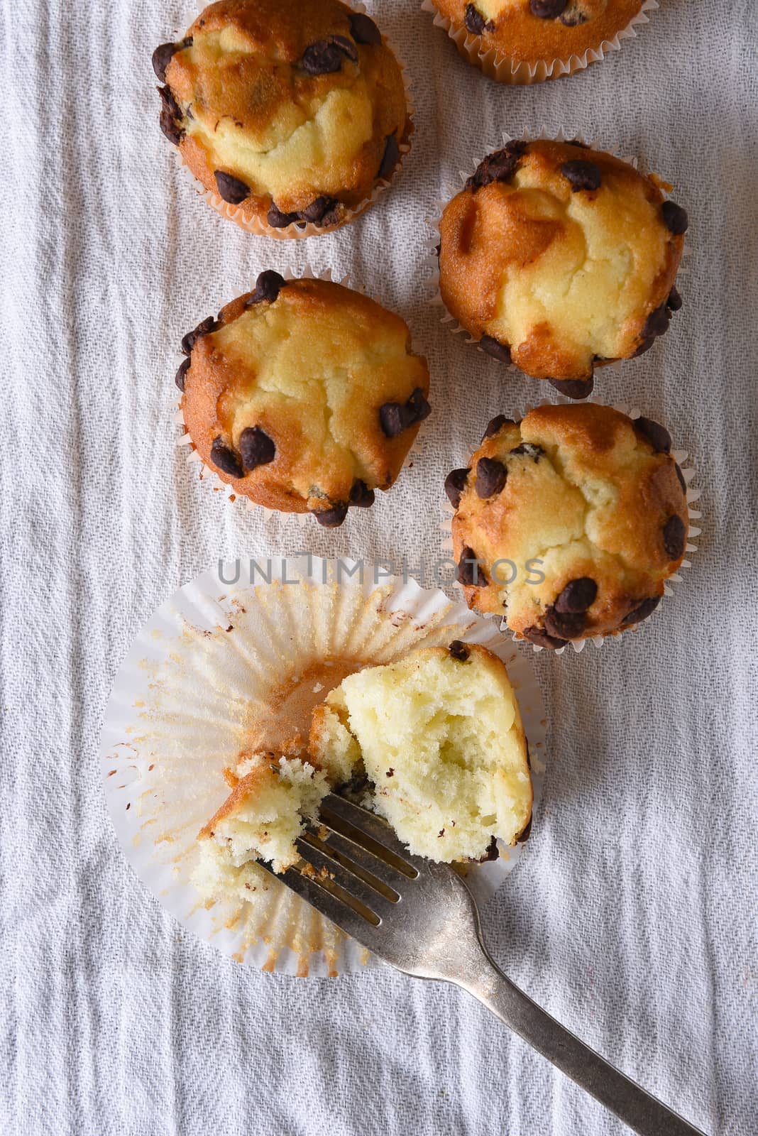 Overhead view of a group of mini chocolate chip muffins on a kitchen towel. One muffin is cut into with a fork.