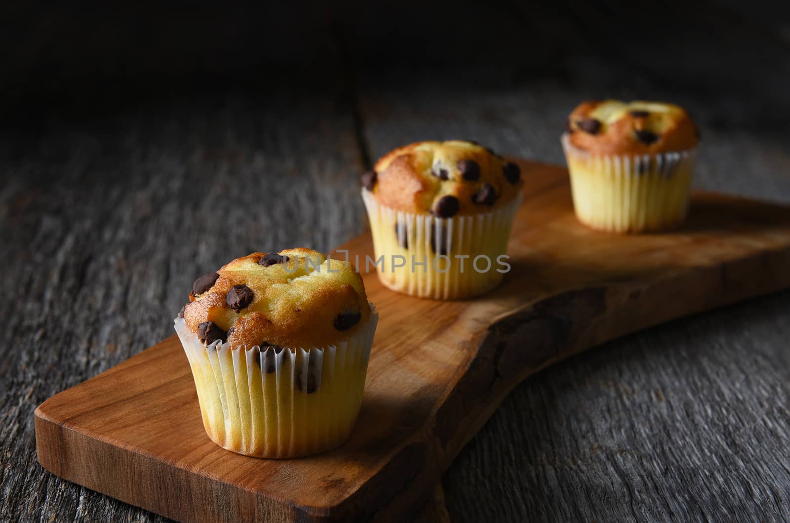 Closeup of three mini chocolate chip muffins on a cutting board by sCukrov