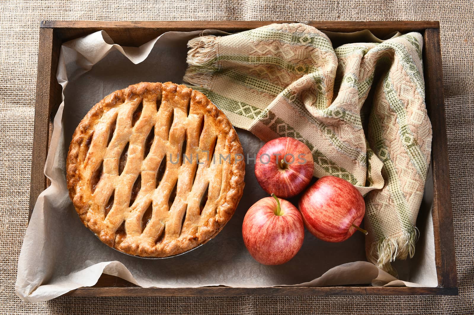 High angle view of a fresh baked apple pie and apples in a wood box on burlap surface.