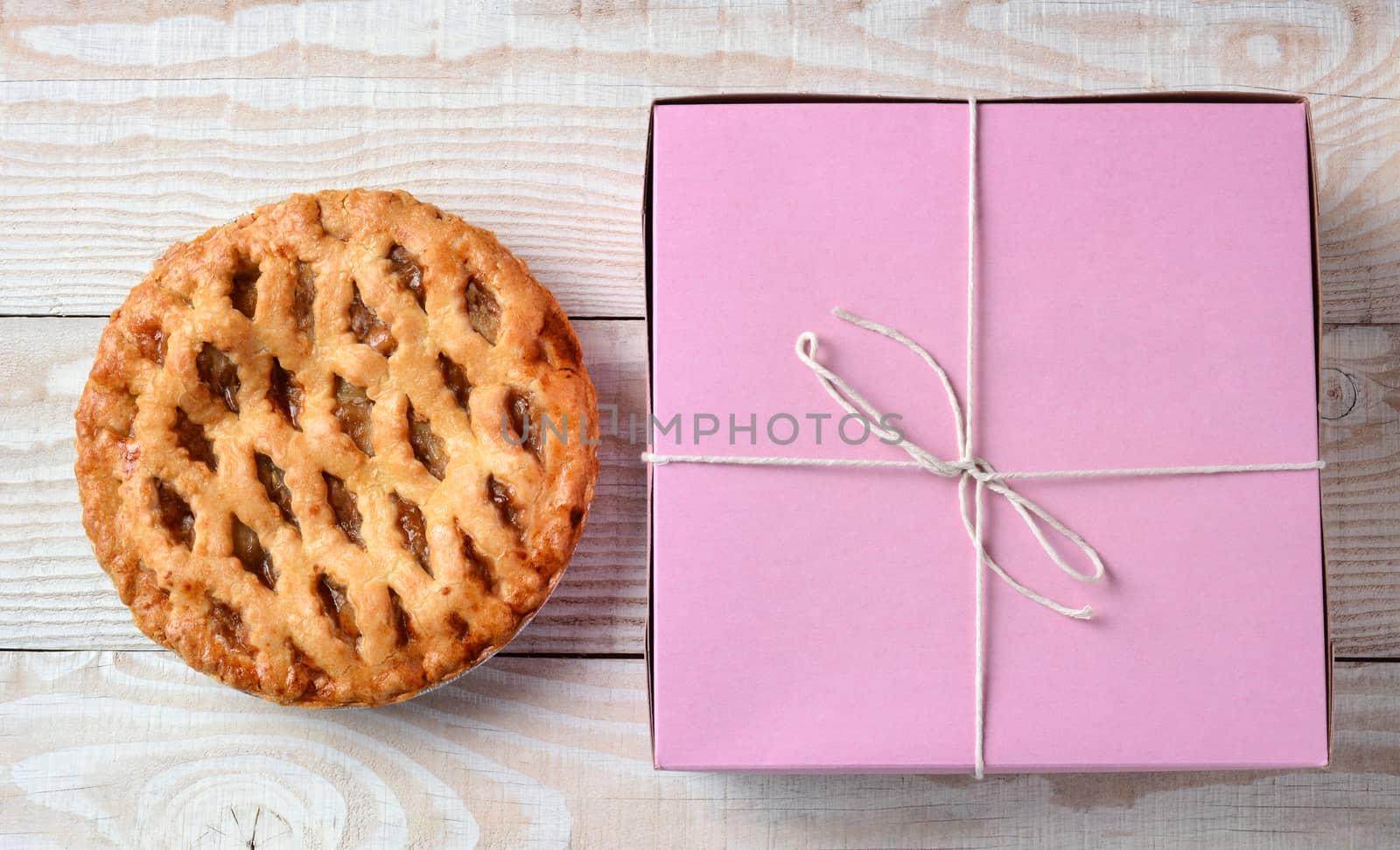 High angle shot of an apple pie and a pink bakery box. Horizontal format on a rustic white wood kitchen table. 