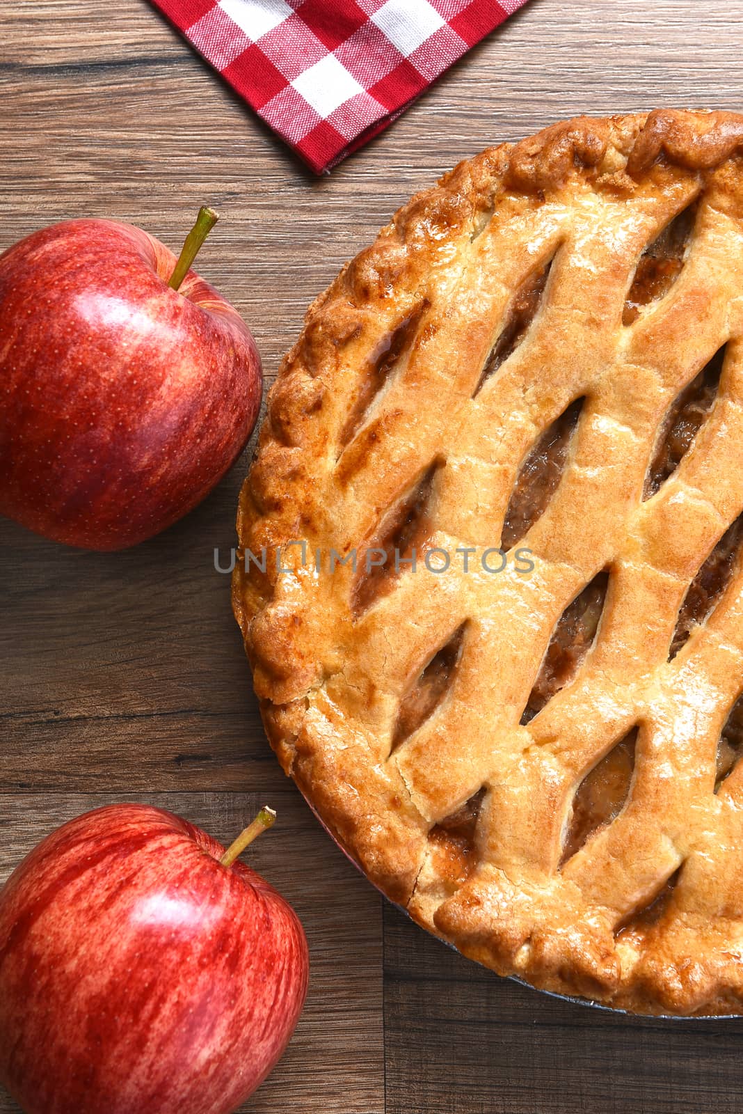 High angle closeup view of a fresh baked apple pie with apples on a rustic wood table. Vertical format.