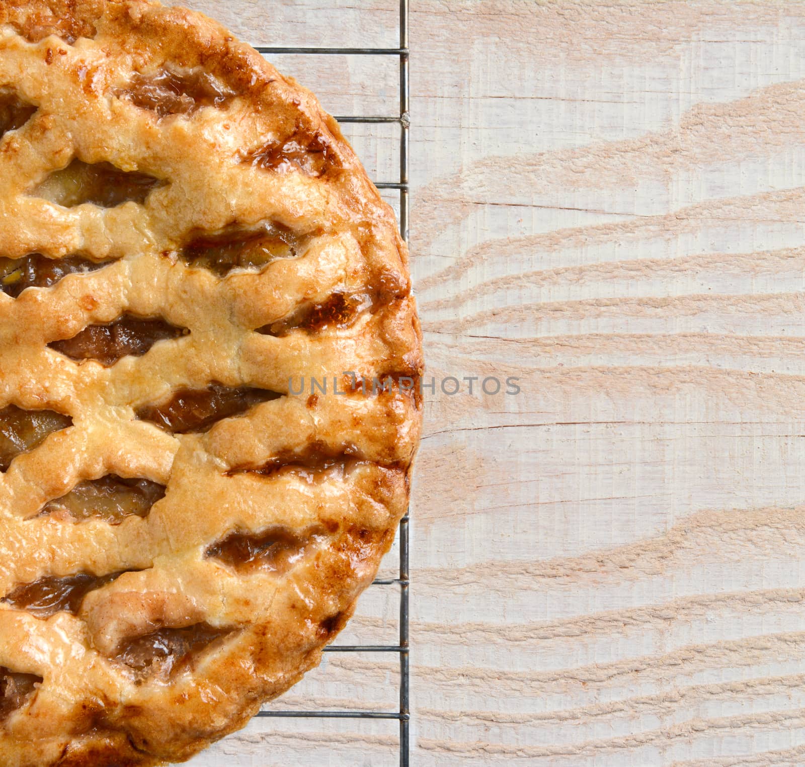 High angle view of a fresh baked holiday apple pie on a cooling rack atop a rustic wood kitchen table. Only half the pie is shown leaving copy space. 