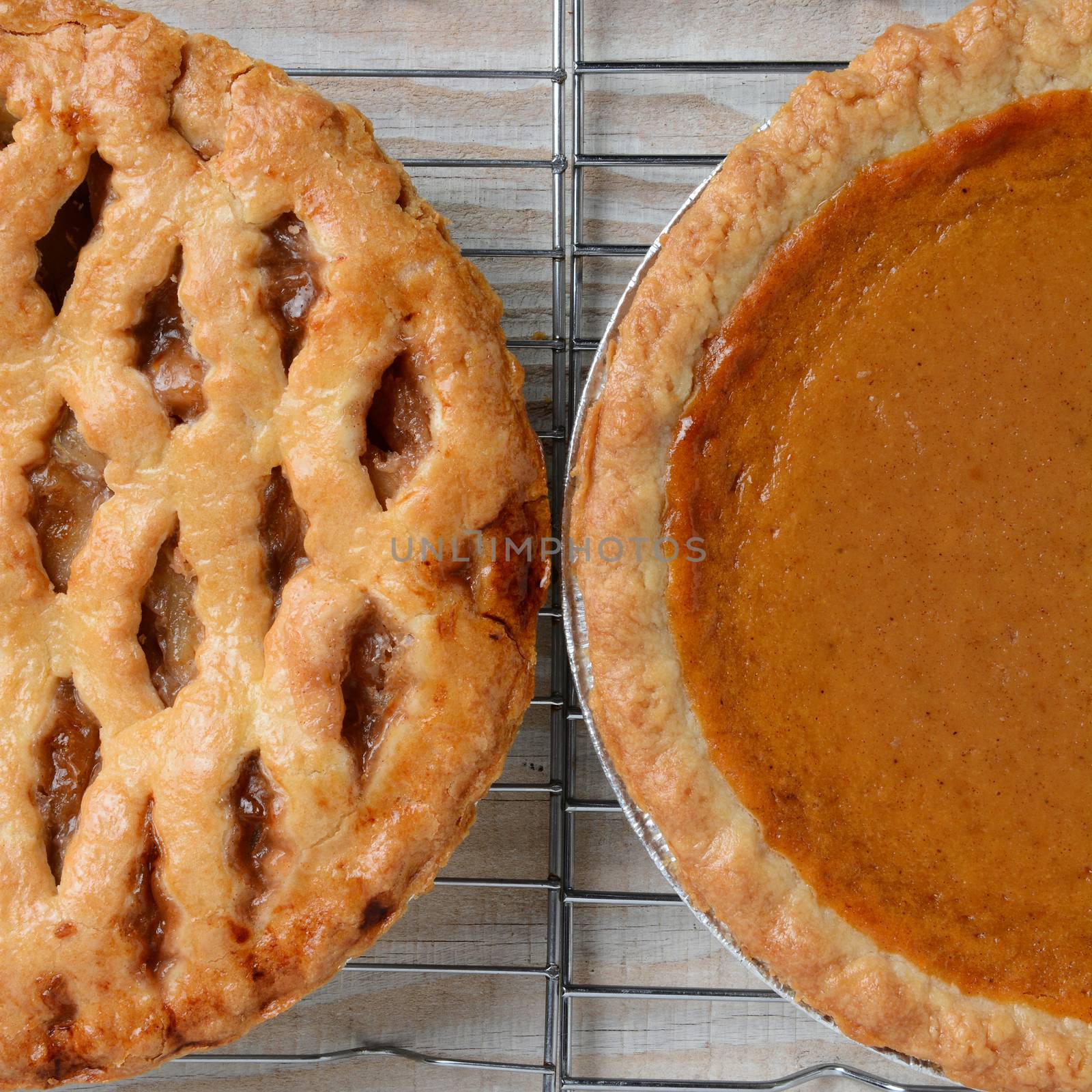 Closeup of holiday Apple and Pumpkin Pies on cooling racks. Only half of each pie is shown. Square format.