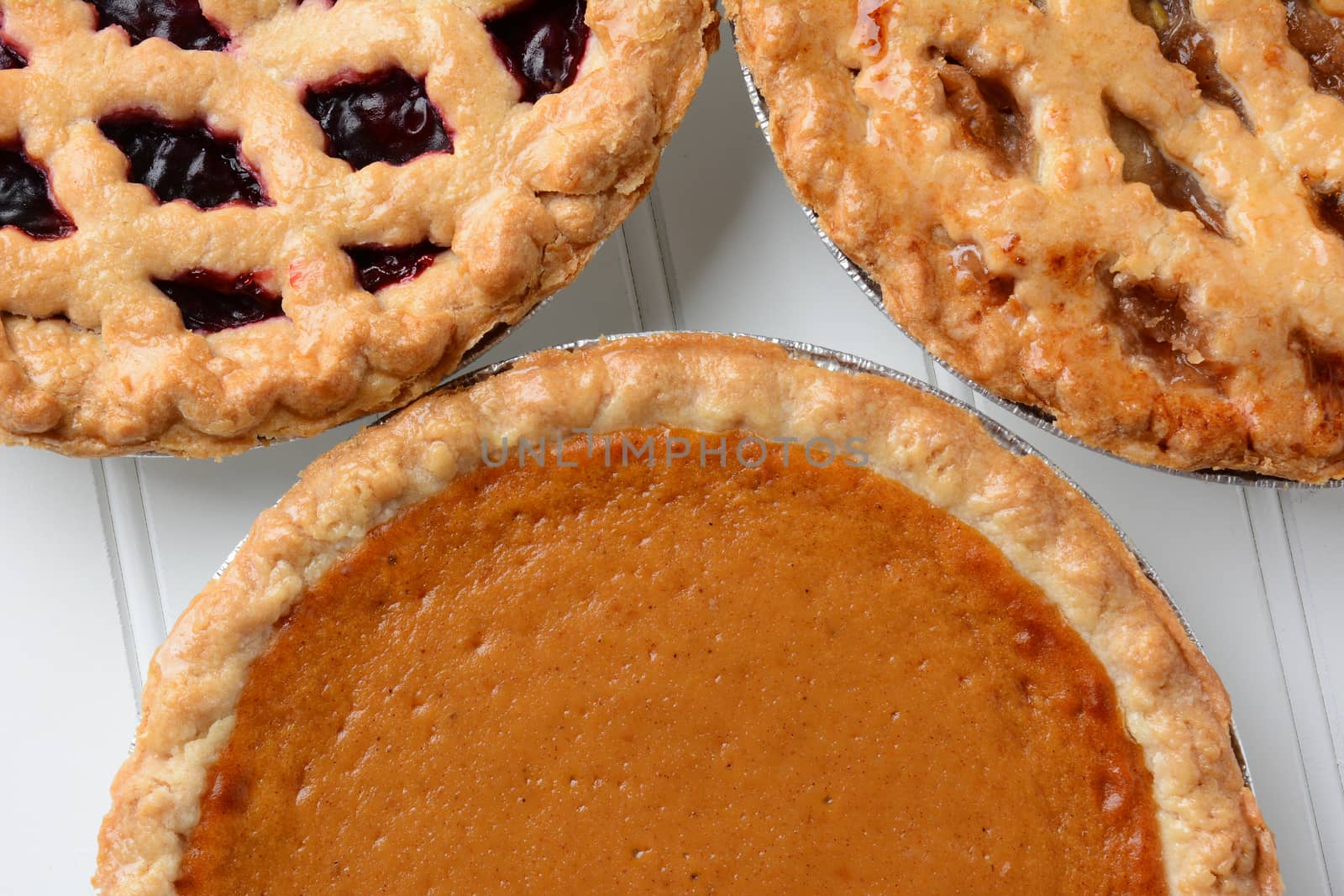 Closeup of three different fresh baked holiday pies.  Pumpkin, apple and a berry pie are shown.