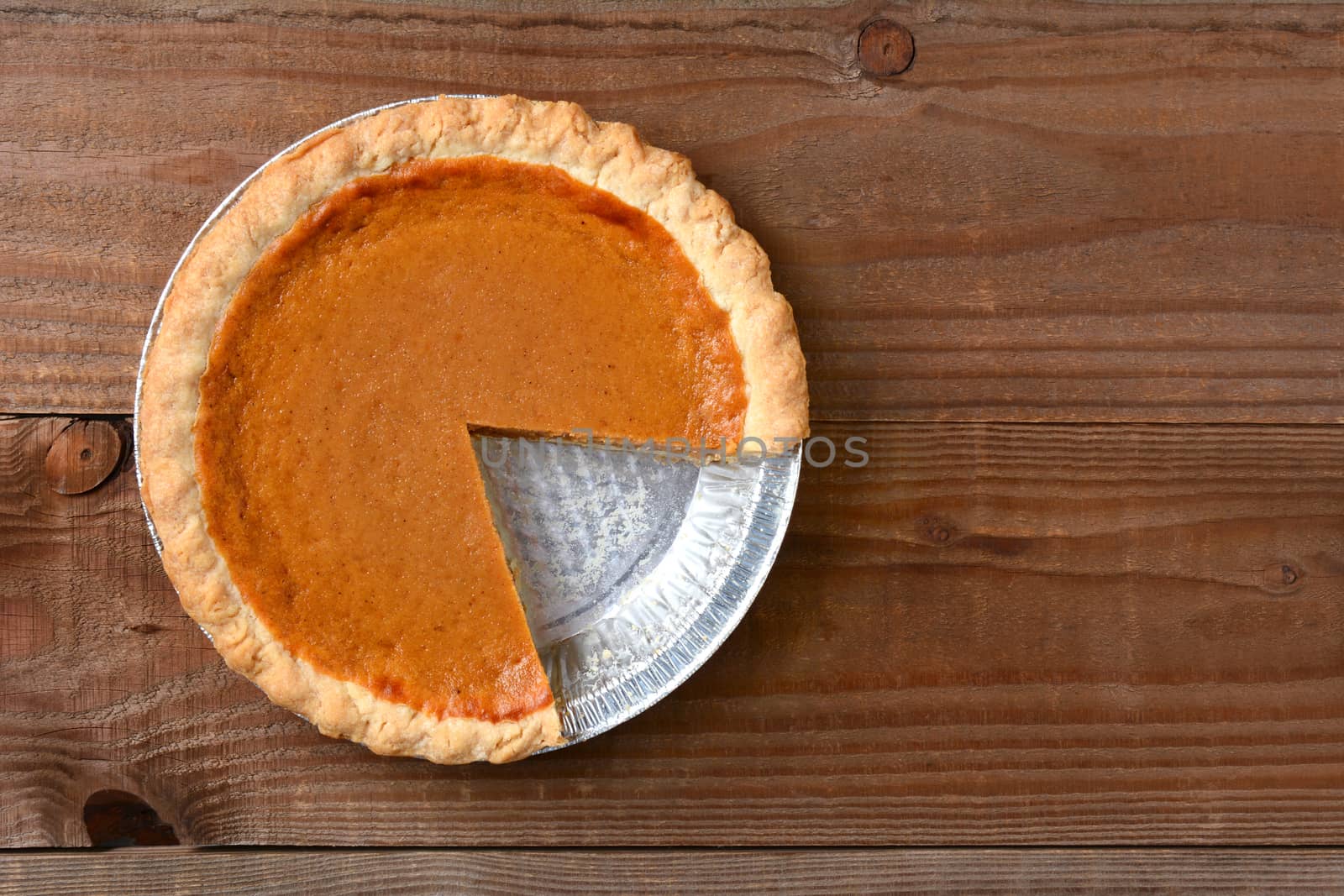 A pumpkin pie with a slice cut out. Horizontal format on a rustic wood table. 