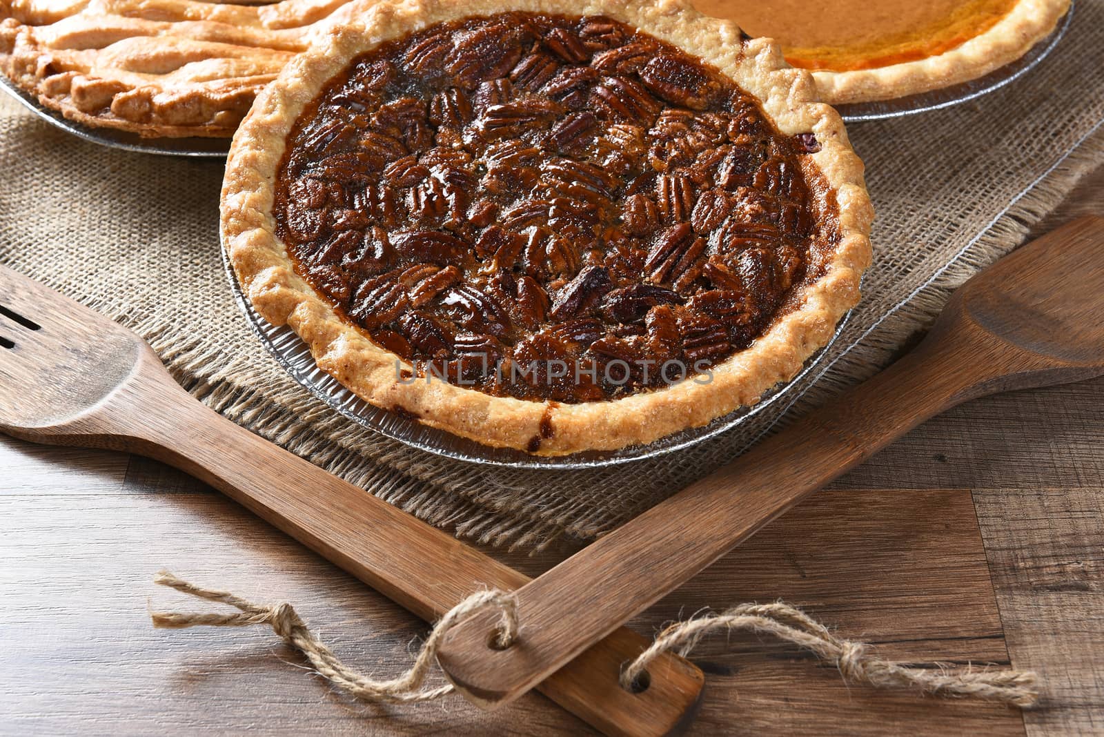Closeup of a fresh baked Pecan pie with wood utensils and burlap table cloth. Two additional pies in the background. Thanksgiving concept.
