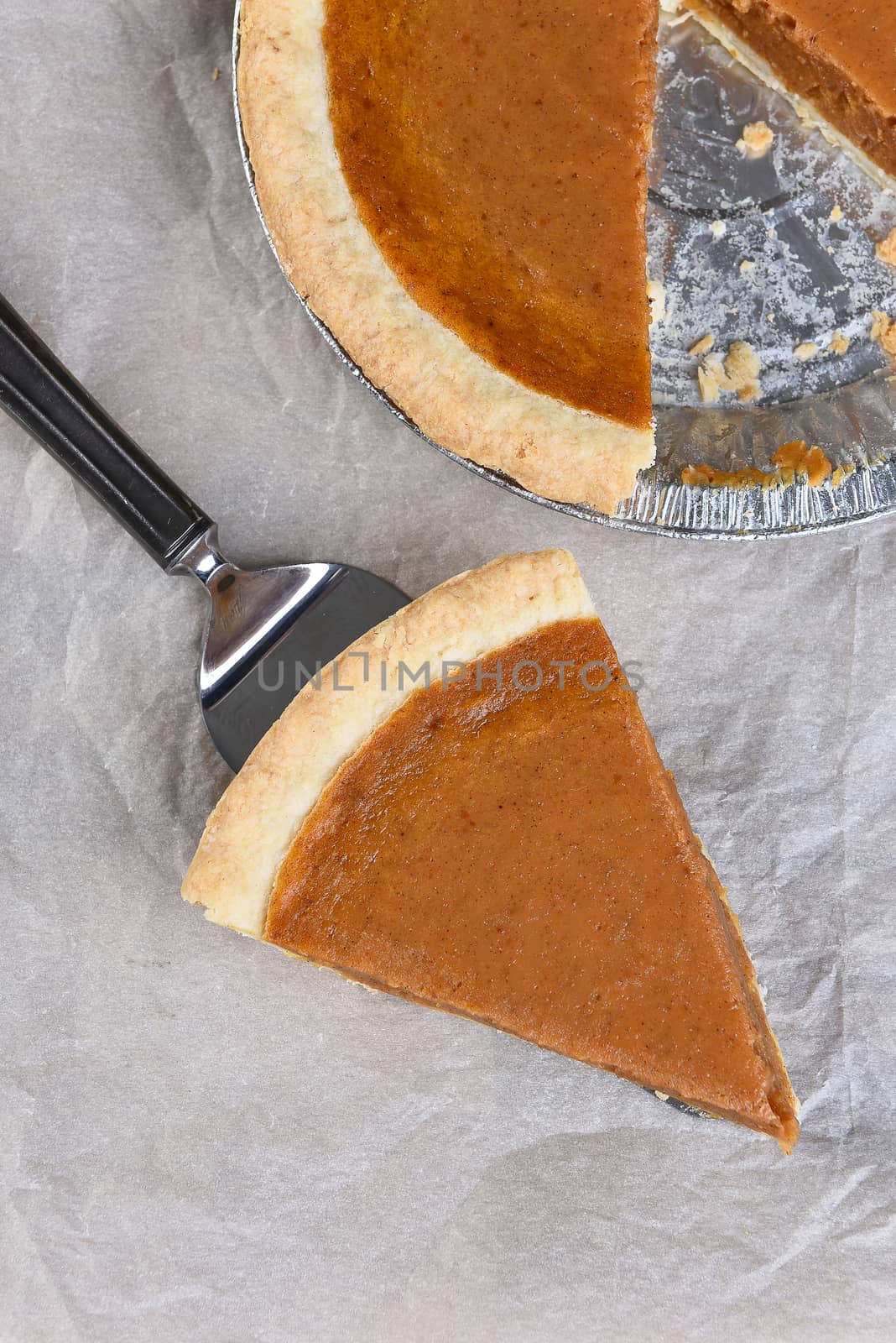 Fresh Baked Pumpkin Pie slice on a server. High angle shot with the rest of the pie in the background.
