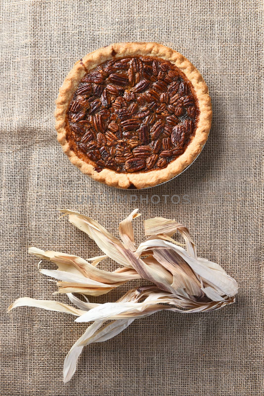 Vertical high angle view of a pecan pie on burlap with corn husks.