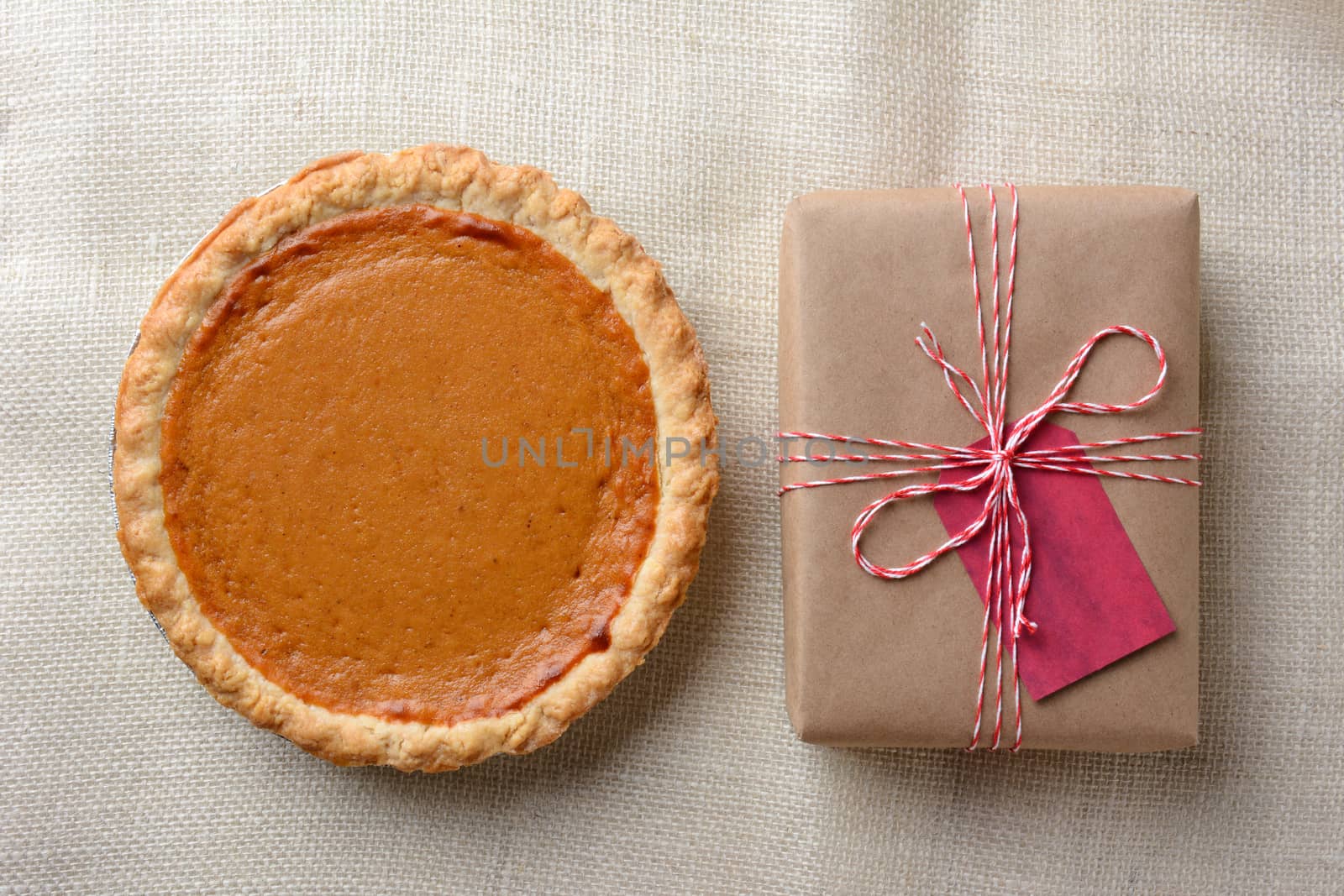 High angle shot of a holiday pumpkin pie and plain paper wrapped present. The brown gift is tied with red and white string and has a red gift tag. Horizontal format.