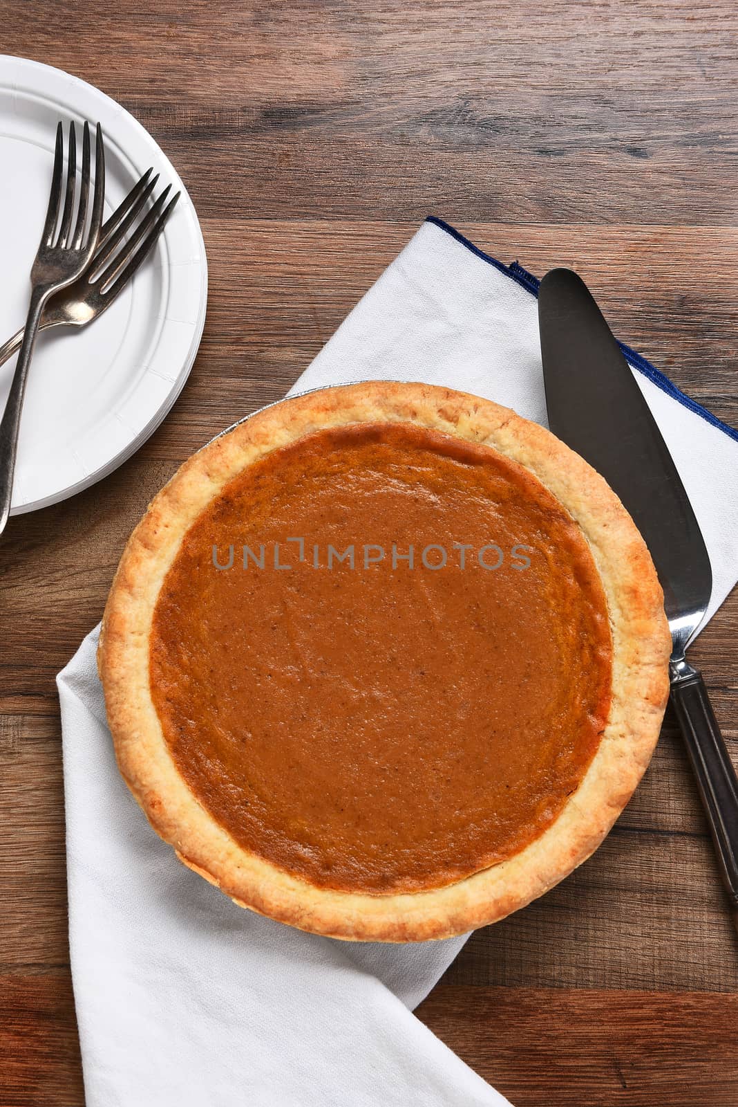 High angle vertical view of a pumpkin pie, server with plates and forks. The dessert is part of a typical Thanksgiving Day Feast.