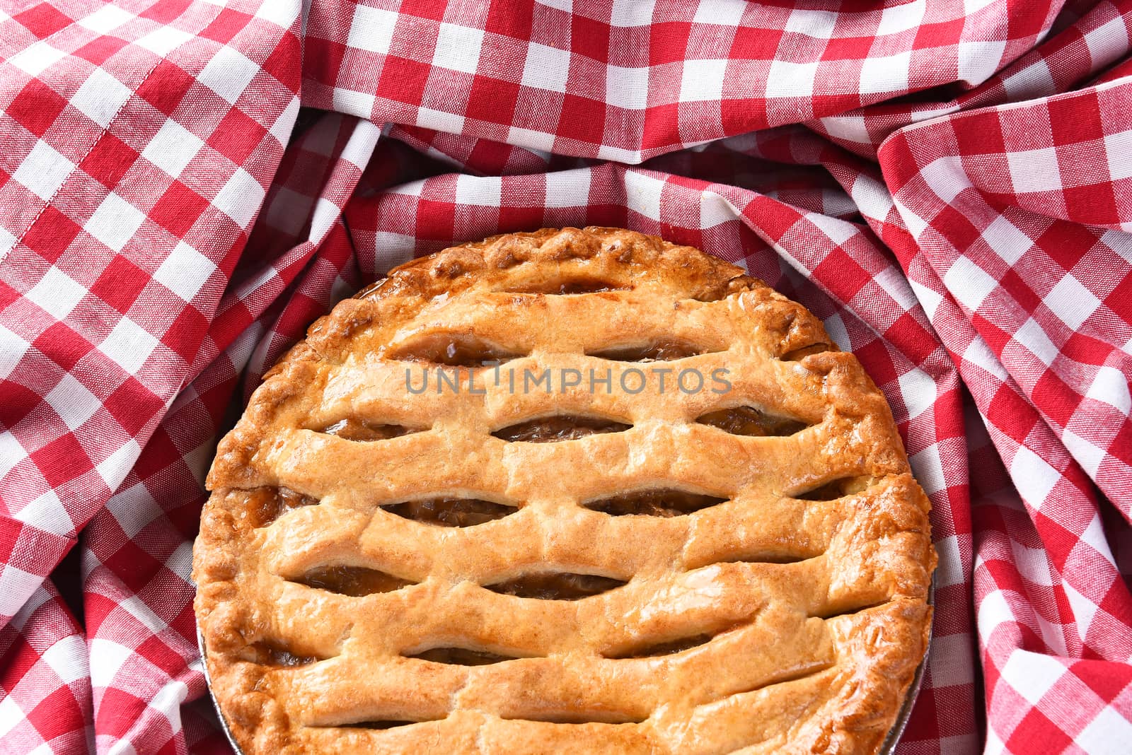 Closeup of a fresh baked Apple Pie surrounded by a red and white checked table cloth. 