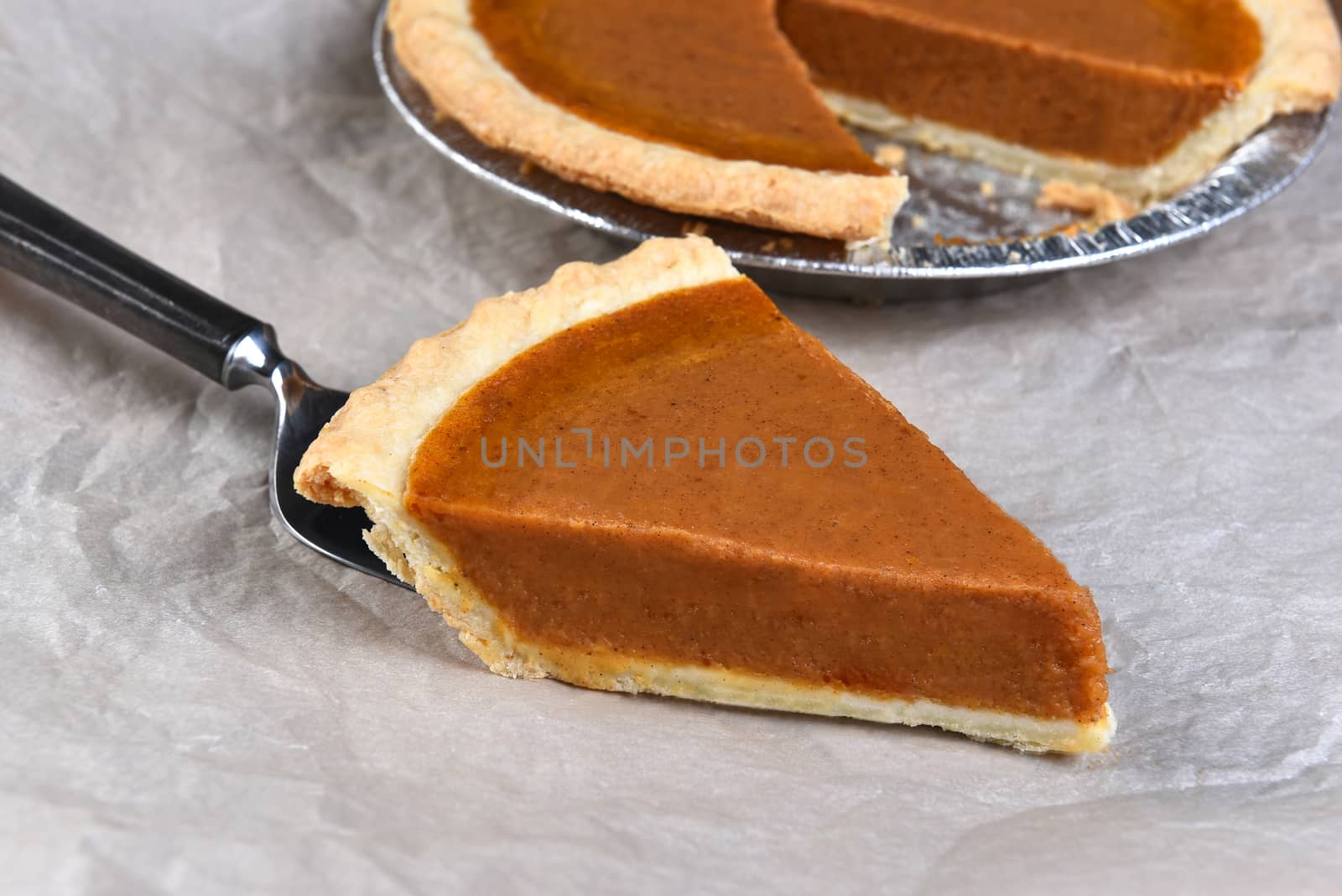 Closeup of a slice of Pumpkin Pie on a spatula with the cut pie in the background.