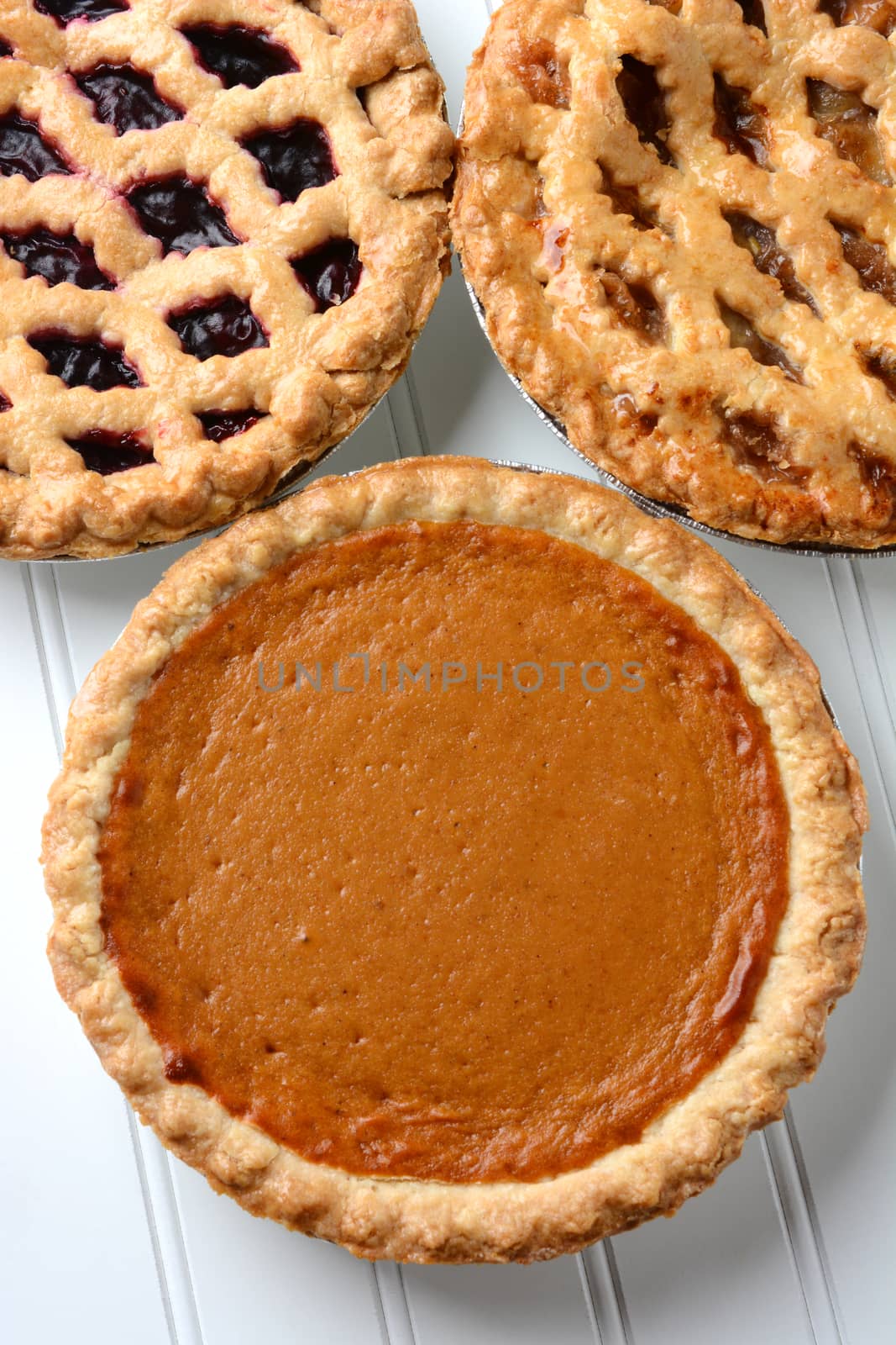 High angle closeup of three fresh baked holiday pies. The traditional American desserts - Pumpkin, Cherry and Apple pie are Thanksgiving staples. Vertical format.