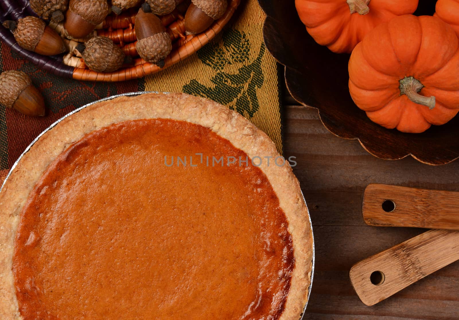 Overhead view of a fresh baked pumpkin pie ready for Thanksgiving. The pie is surrounded by autumn accessories including acorns, and mini pumpkins. Horizontal format.