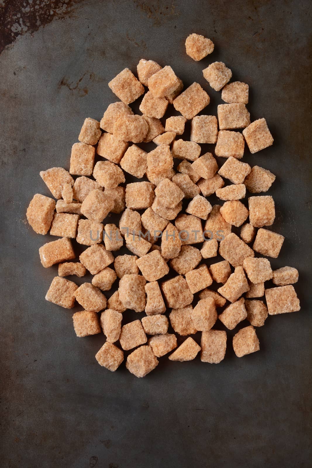 High angle view of a pile of brown natural sugar cubes on a used metal baking sheet. Vertical format.
