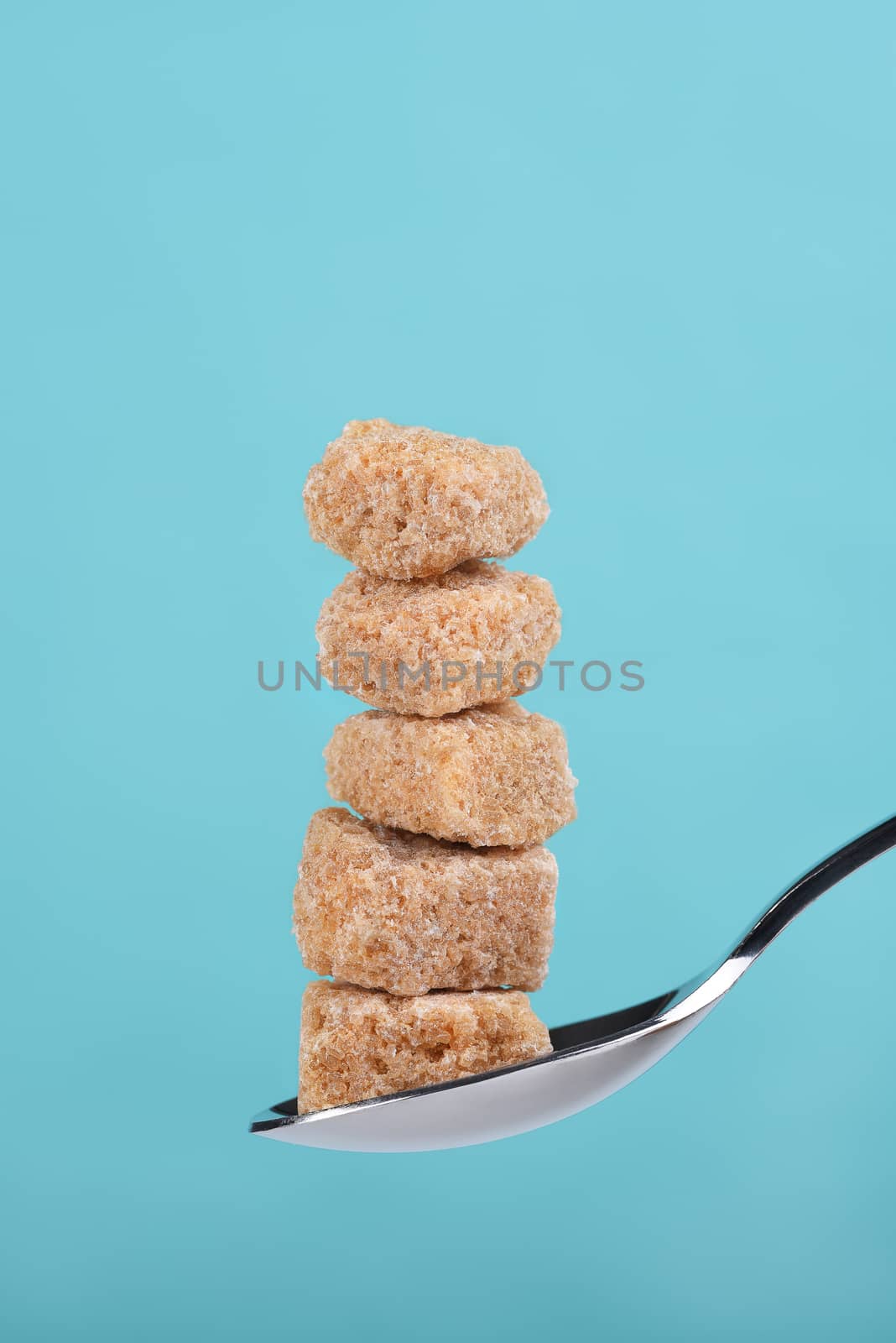 Closeup of 5 Raw Brown sugar cubes stacked on a spoon against a teal background.