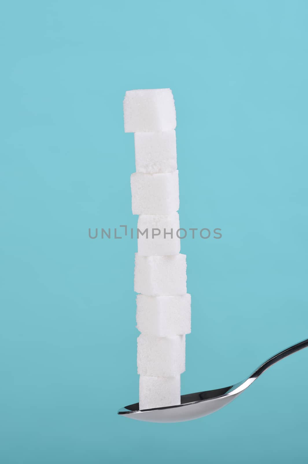 Closeup of several sugar cubes stacked on a spoon against a teal background.