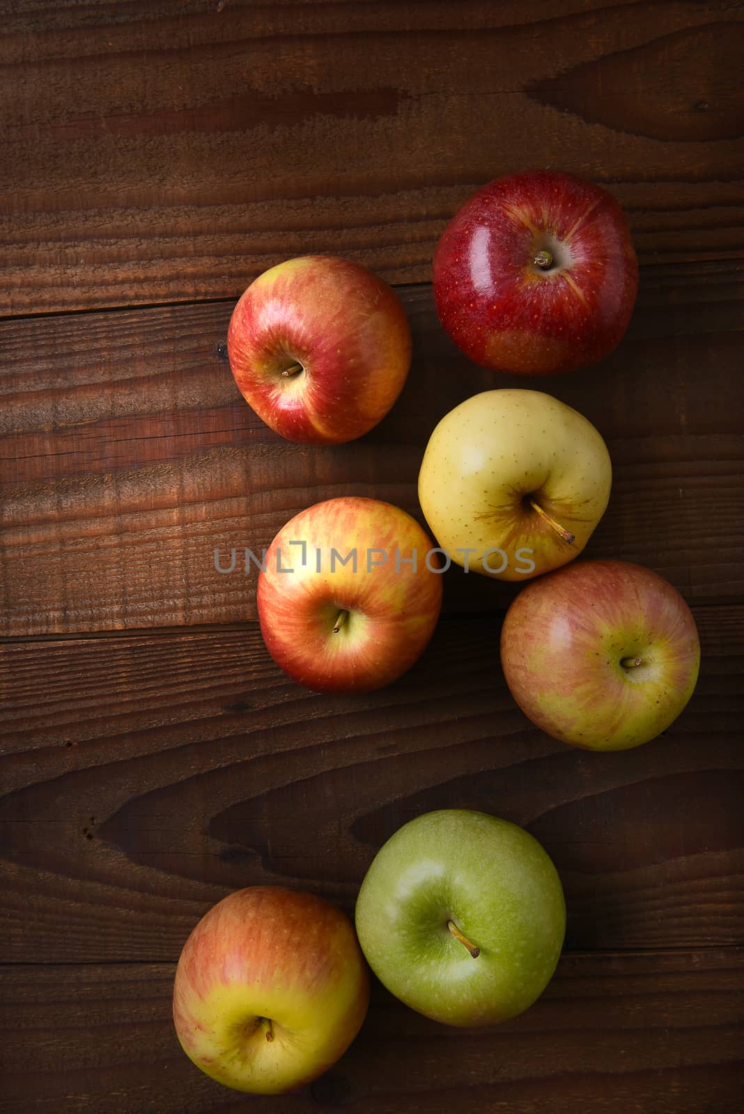 Different varieties of fresh picked apples on a rustic wood table. Fuji, Gala, Granny Smith, Braeburn, Golden Delicious Shot from a high angle.