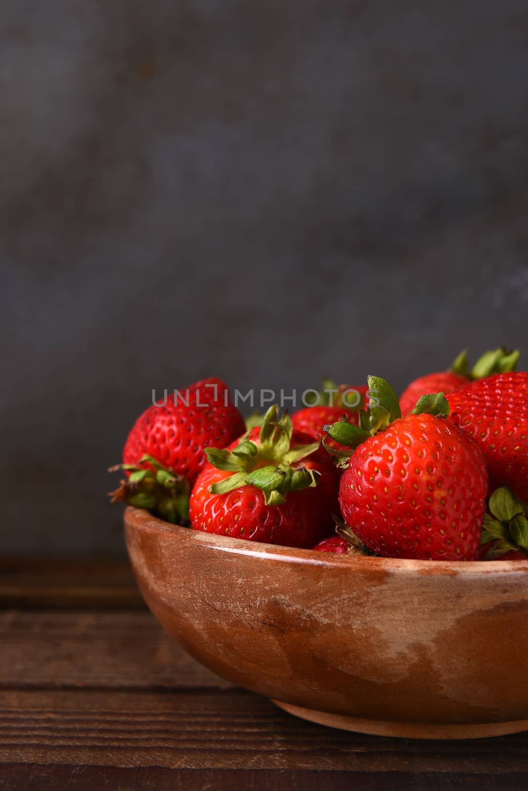 Still life of a bowl full of fresh picked strawberries on a wood table. Vertical format with copy space.