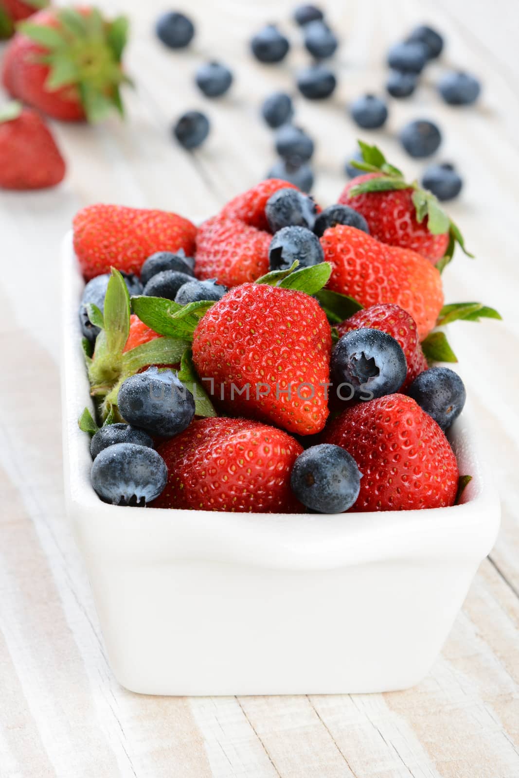 White Bowl of Strawberries and Blueberries on Rustic Table by sCukrov