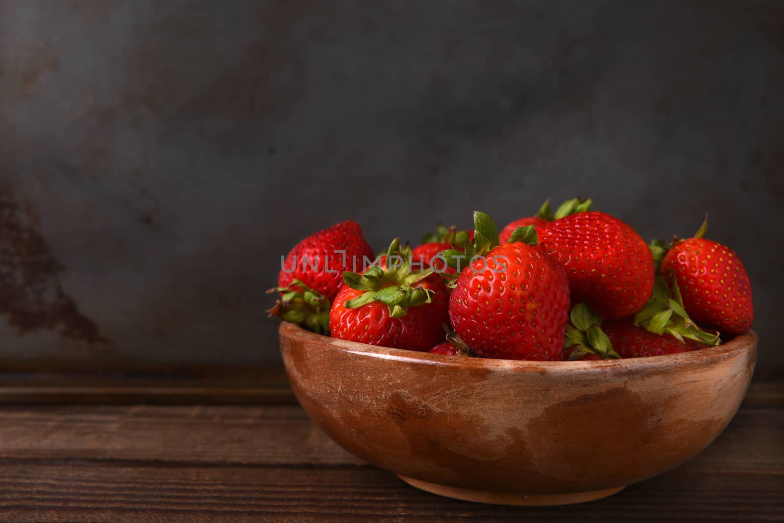Horizontal still life of a bowl full of fresh picked strawberries on a wood table. Horizontal format with copy space.